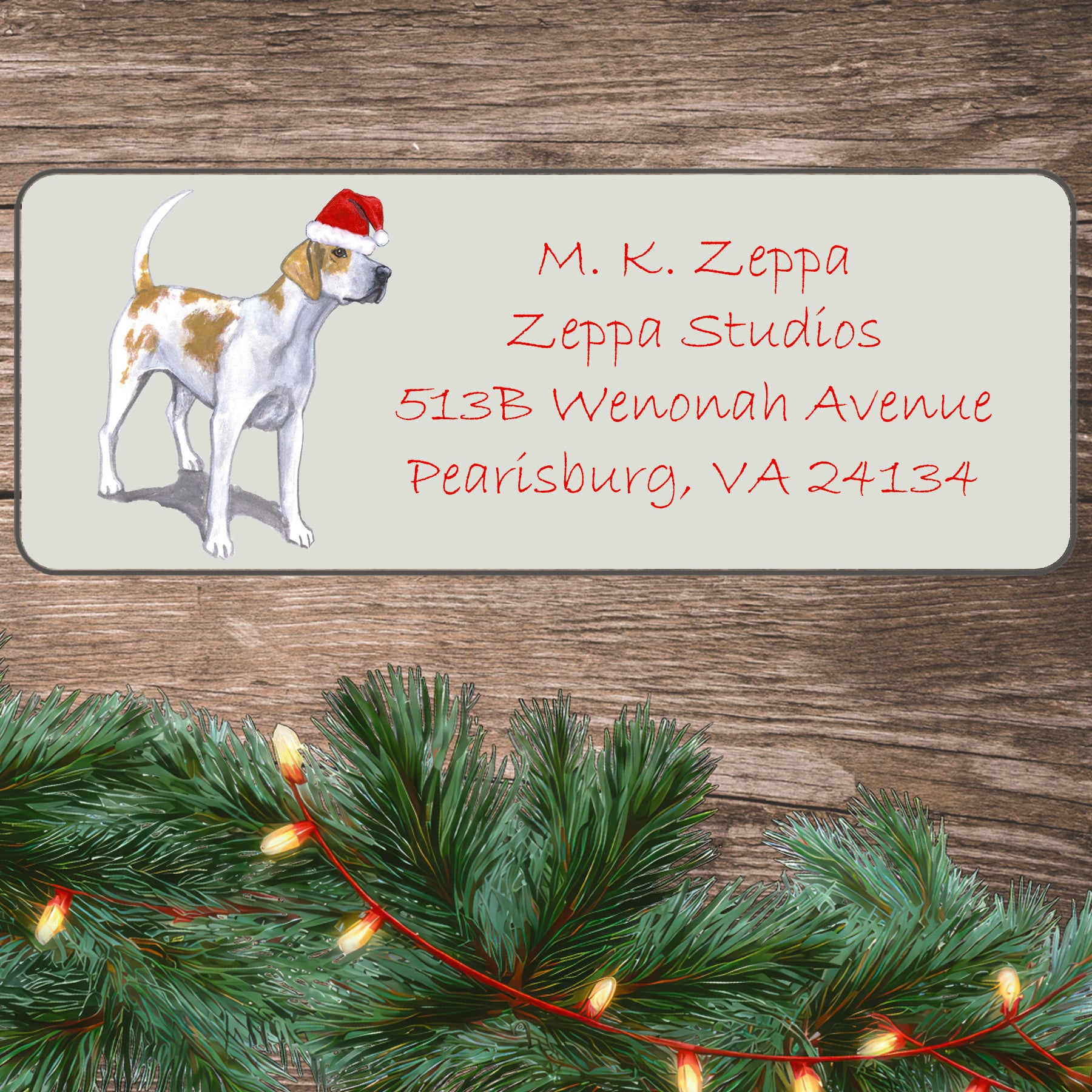 An English Foxhound in a Santa Hat illustration on an ivory return address label set off by a wood surface with holiday greenery background.