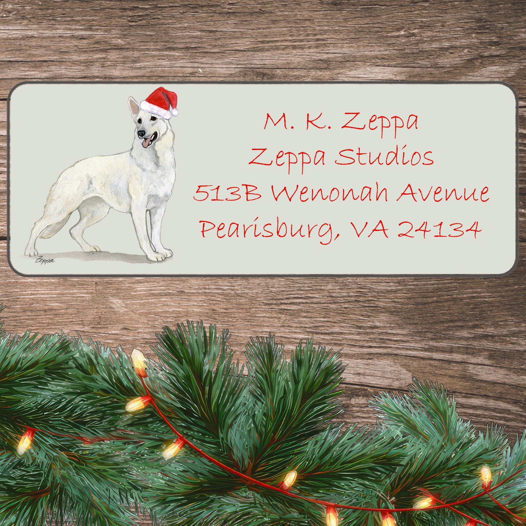 An illustration of a white German Shepherd wearing a Santa Hat on an ivory return address label set off by a wood surface with holiday greenery background.