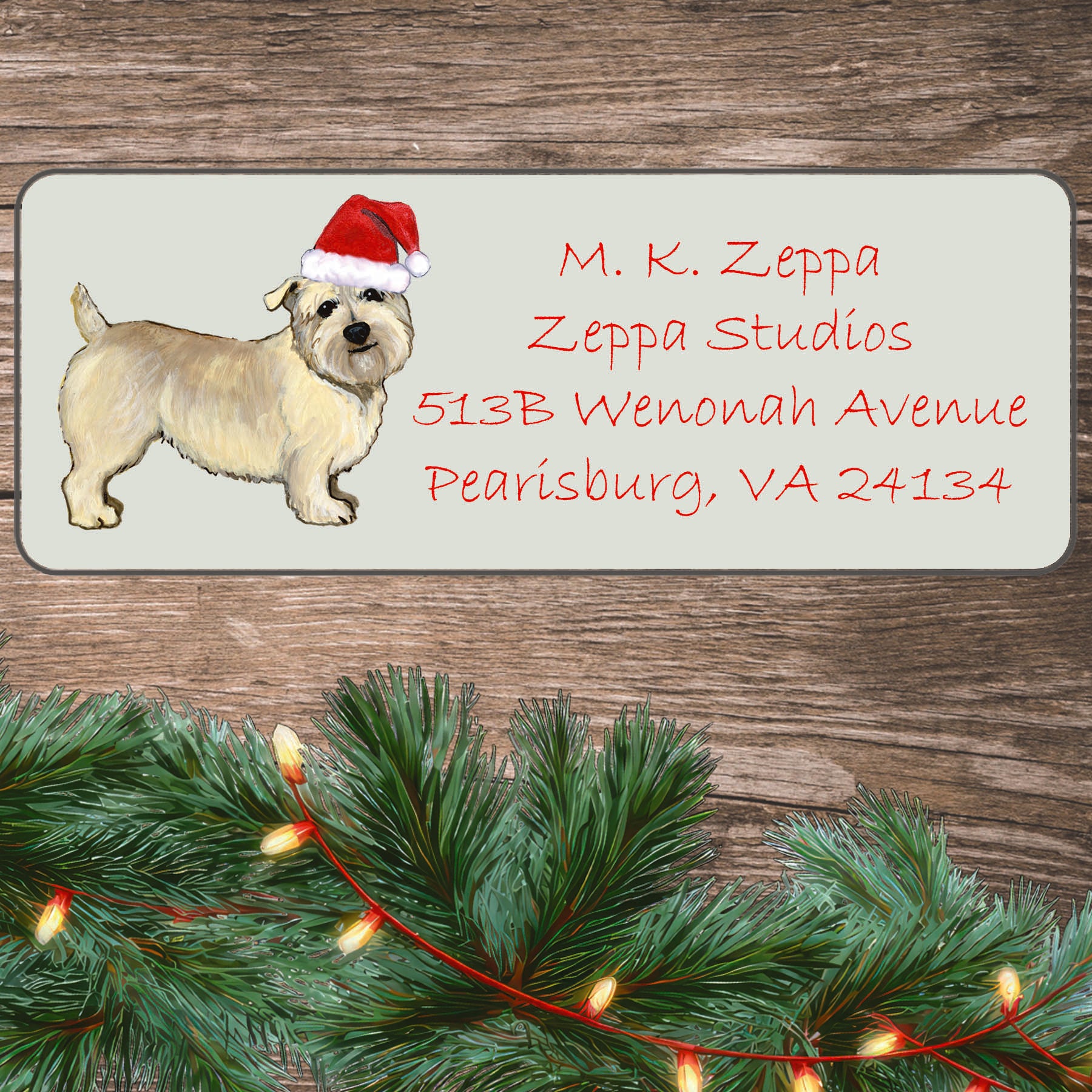 An illustration of a Glen of Imaal Terrier wearing a Santa Hat on an ivory return address label set off by a wood surface with holiday greenery background.