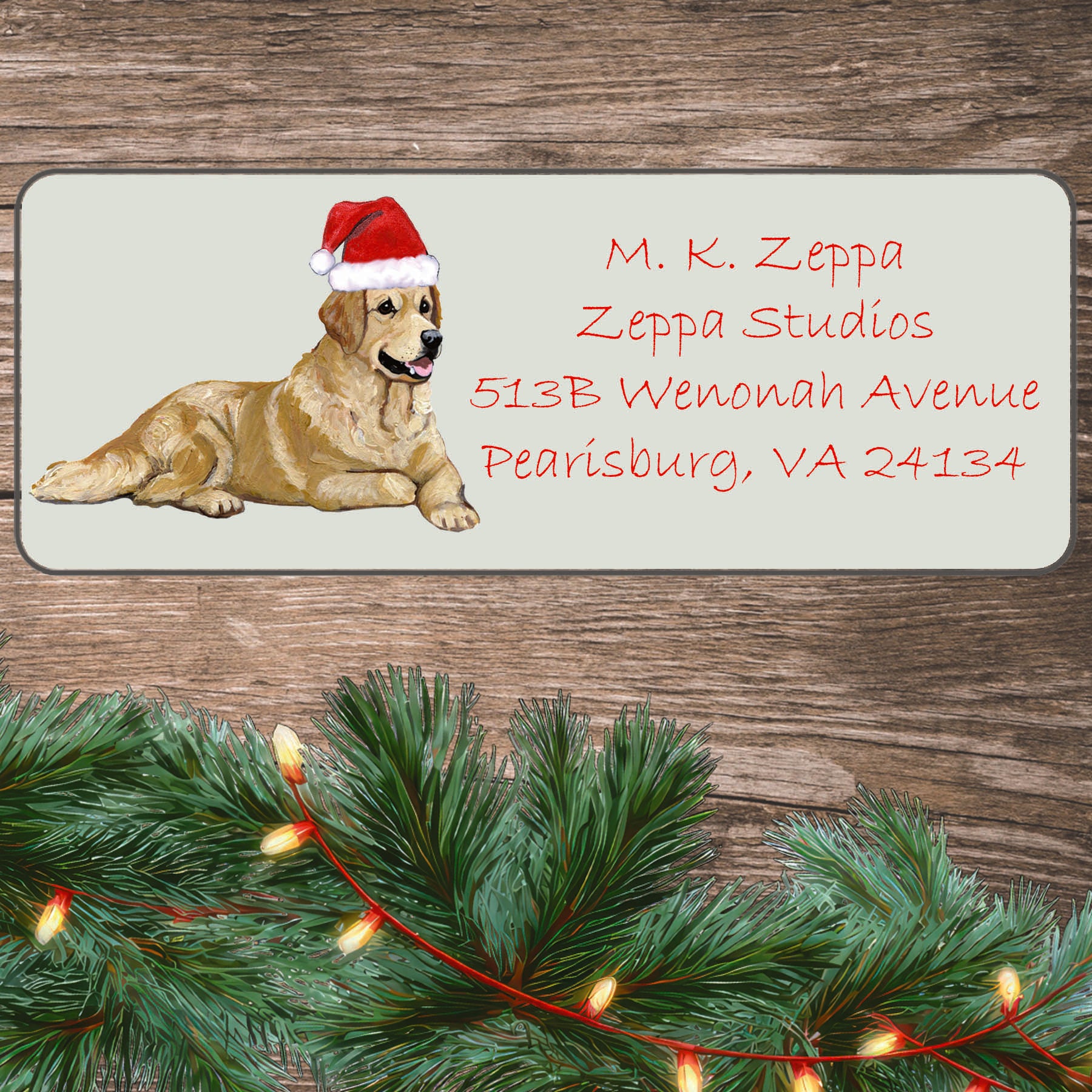 An illustration of a Golden Retriever wearing a Santa Hat on an ivory return address label set off by a wood surface with holiday greenery background.