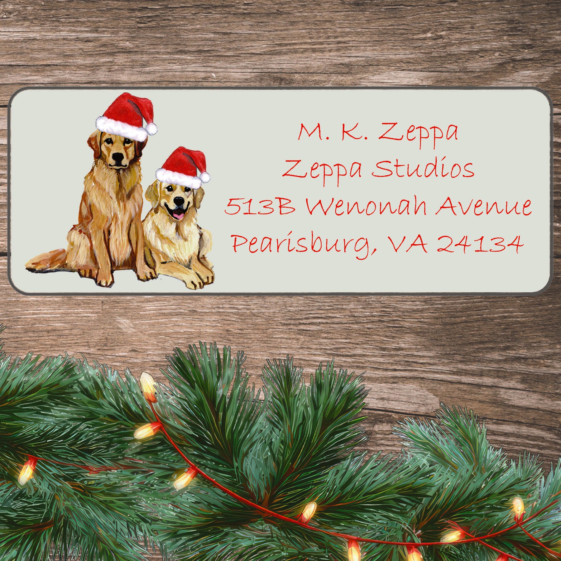 An illustration of a Golden Retriever Pair wearing a Santa Hat on an ivory return address label set off by a wood surface with holiday greenery background.