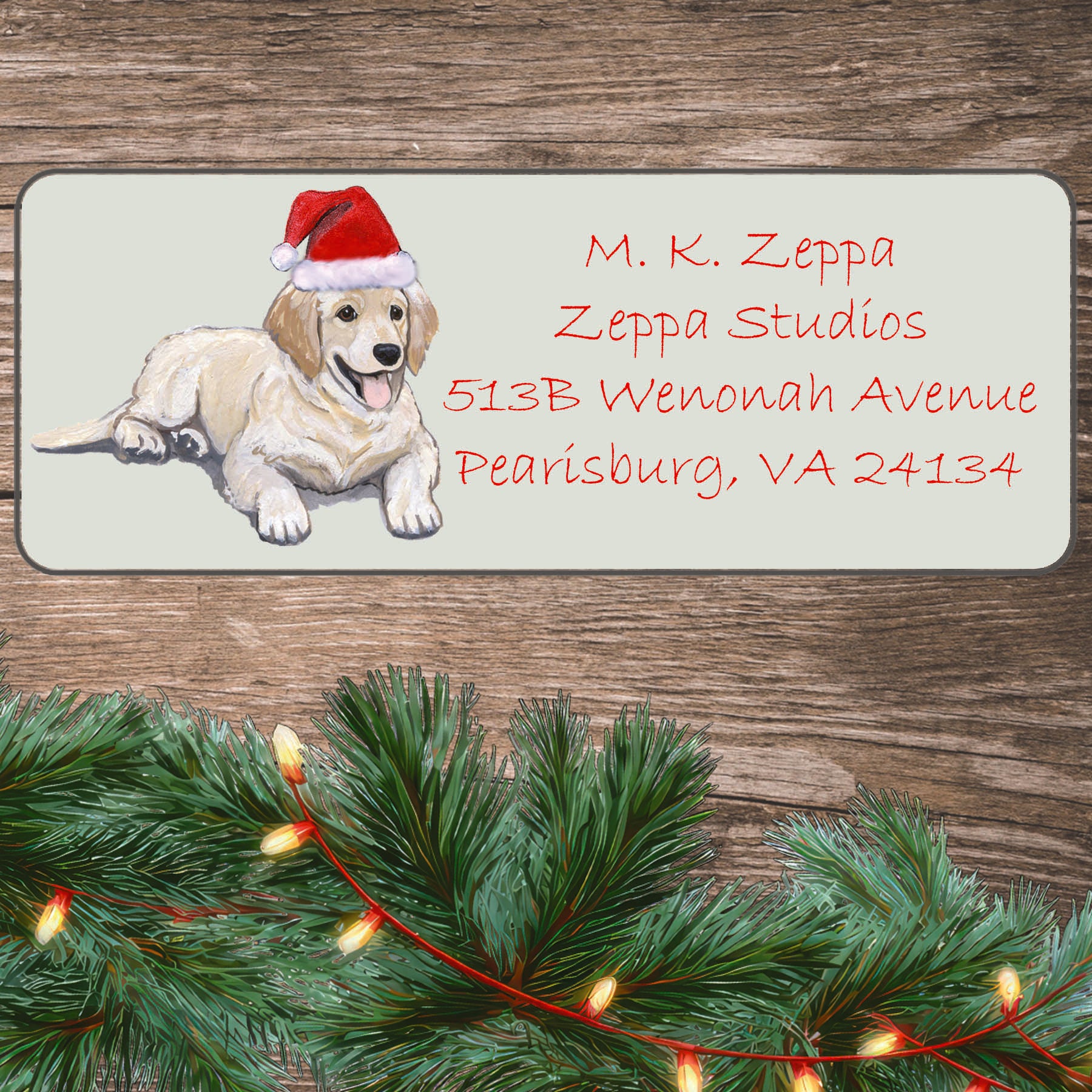 An illustration of a Golden Retriever Puppy wearing a Santa Hat on an ivory return address label set off by a wood surface with holiday greenery background.