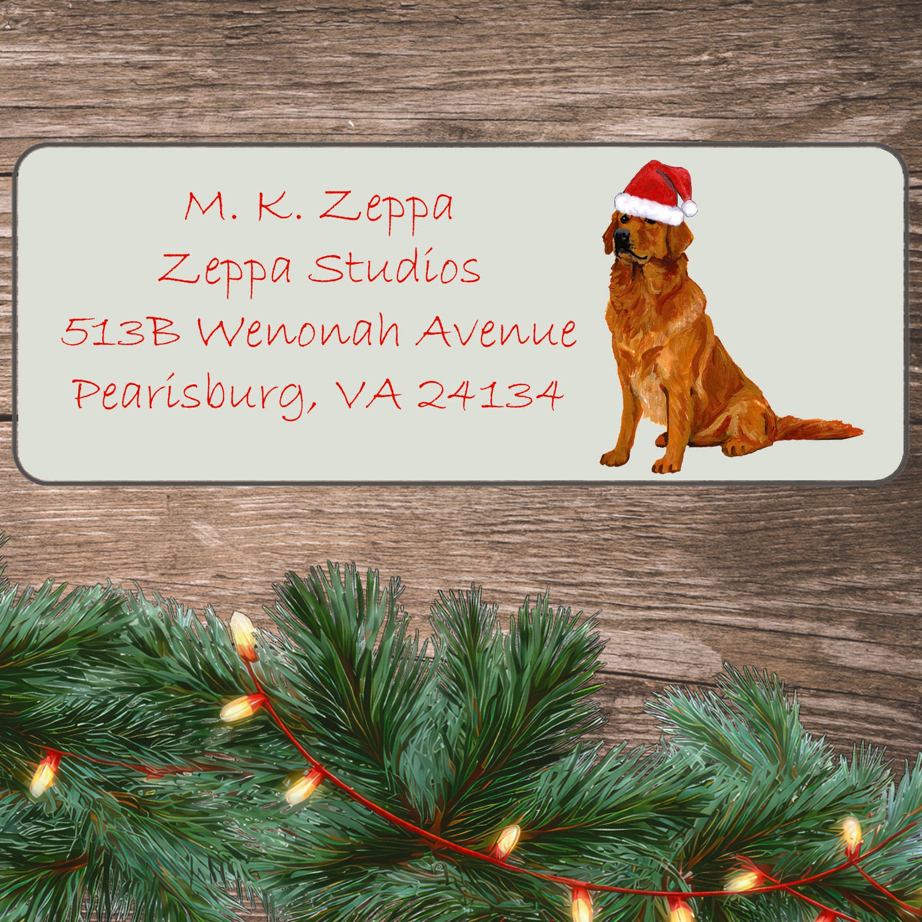 An illustration of a sitting Golden Retriever wearing a Santa Hat on an ivory return address label set off by a wood surface with holiday greenery background.