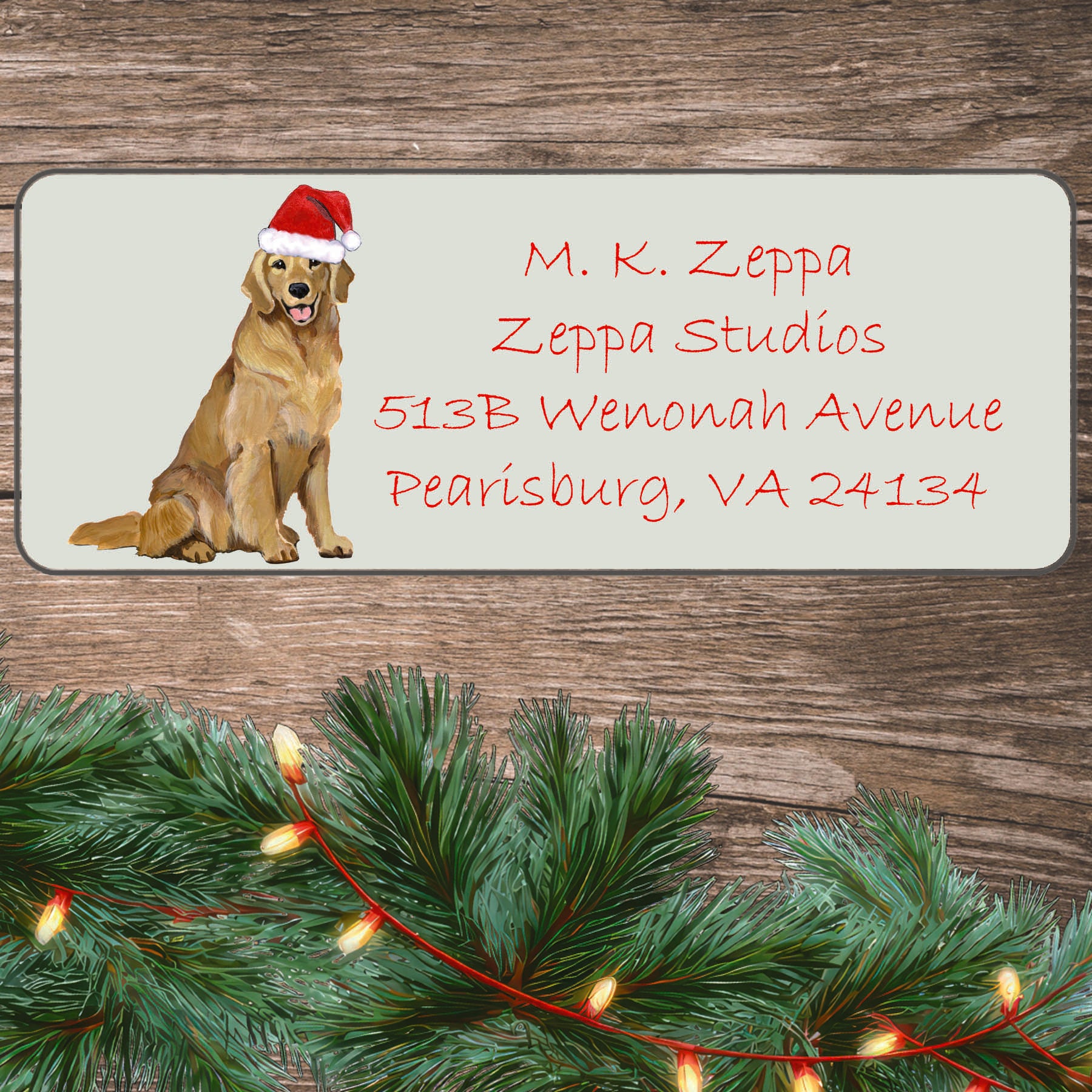 An illustration of a smiling Golden Retriever wearing a Santa Hat on an ivory return address label set off by a wood surface with holiday greenery background.