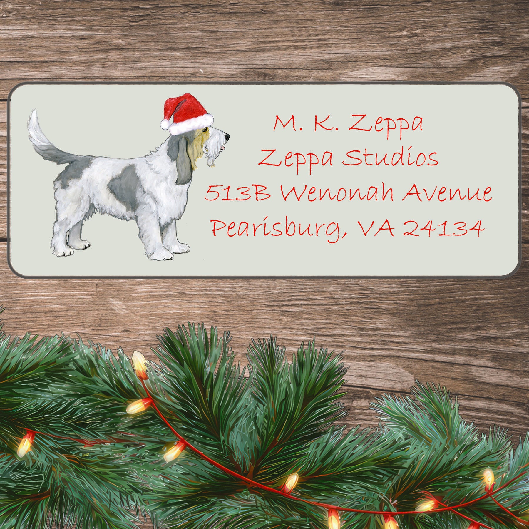 An illustration of a  Grand Basset Griffon Vendeen wearing a Santa Hat on an ivory return address label set off by a wood surface with holiday greenery background.