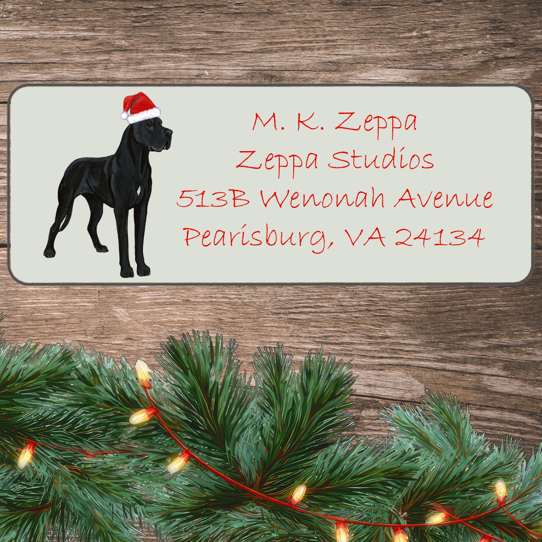 An illustration of a black Great Dane wearing a Santa Hat on an ivory return address label set off by a wood surface with holiday greenery background.