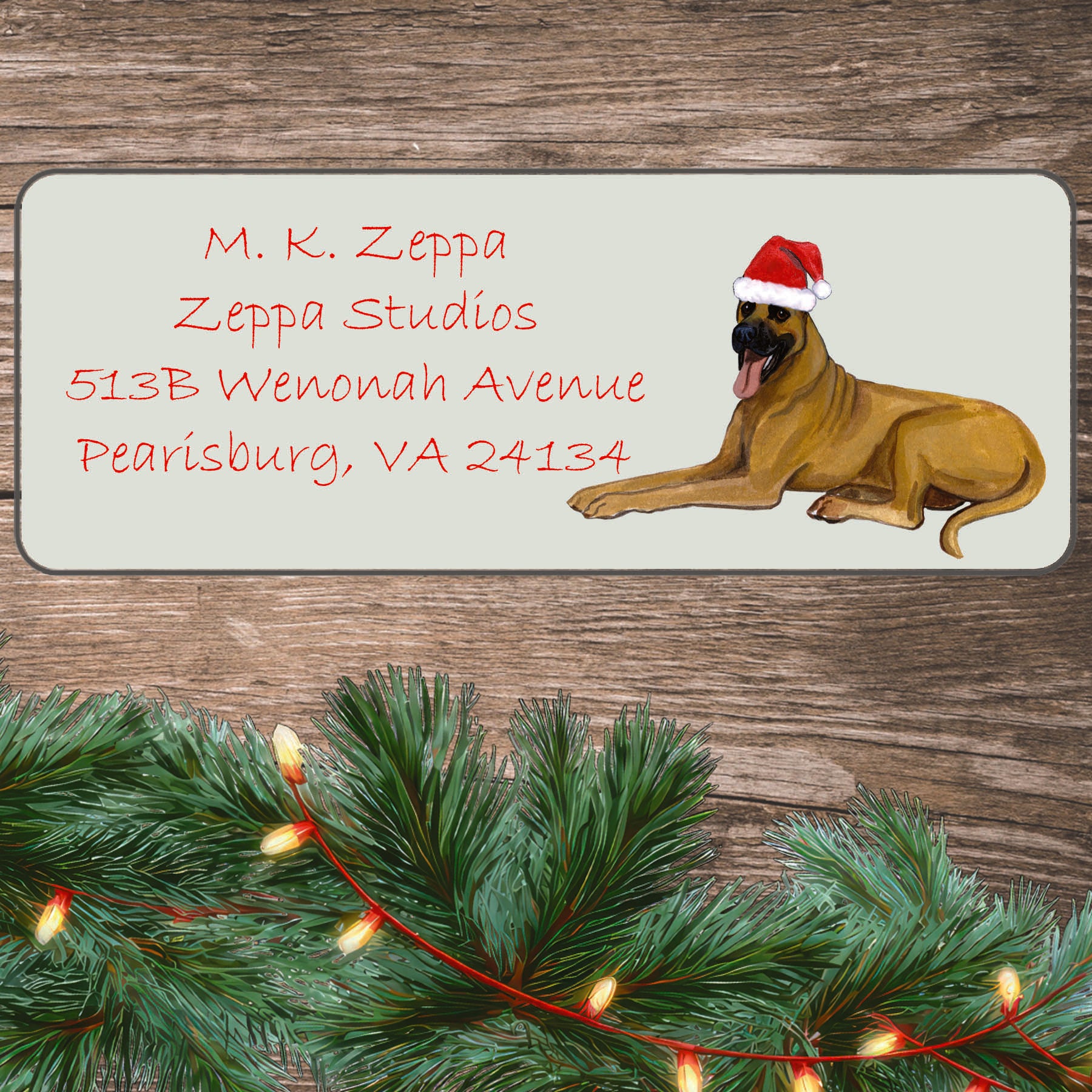An illustration of a Great Dane wearing a Santa Hat on an ivory return address label set off by a wood surface with holiday greenery background.
