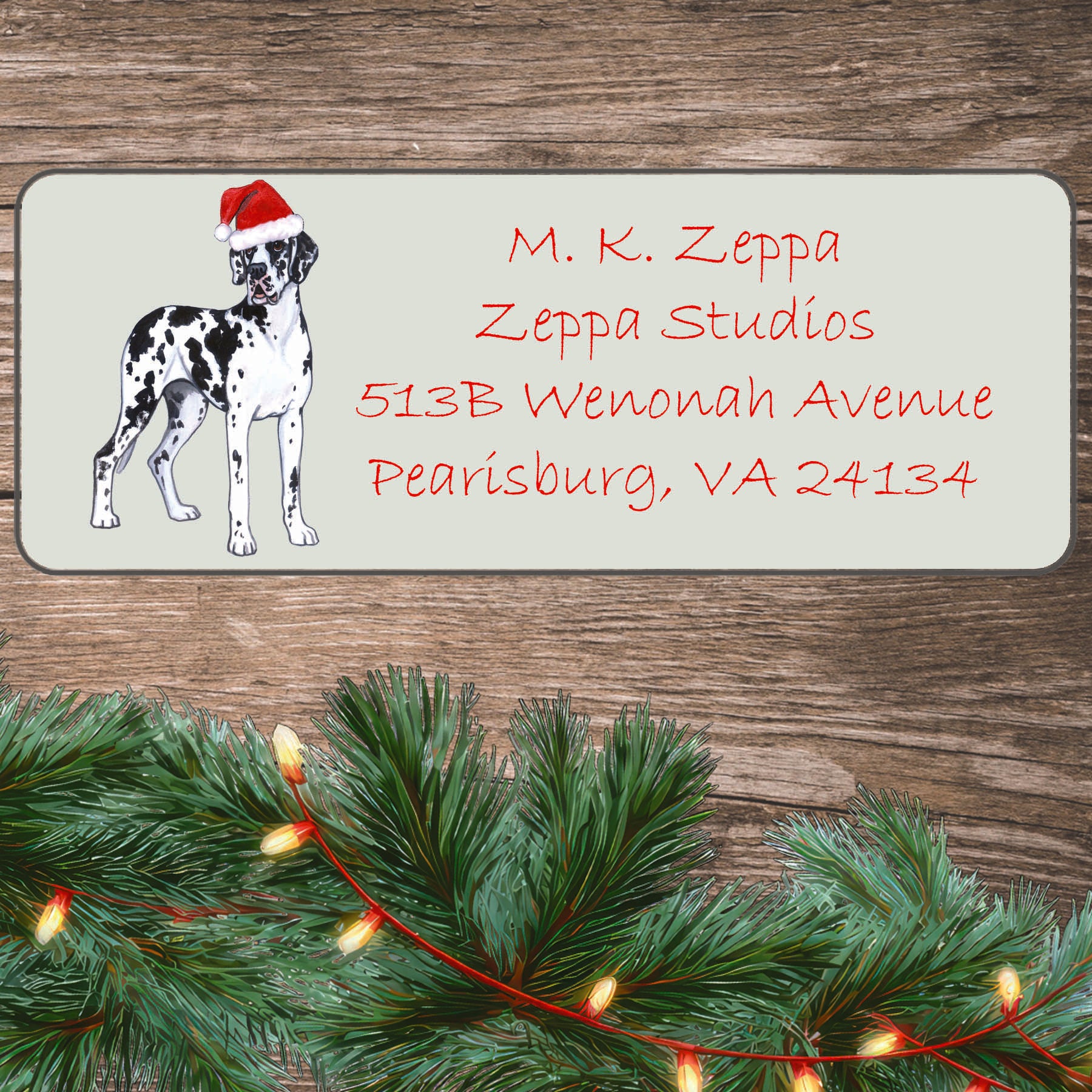 An illustration of a Harlequin Great Dane with Natural Ears wearing a Santa Hat on an ivory return address label set off by a wood surface with holiday greenery background.