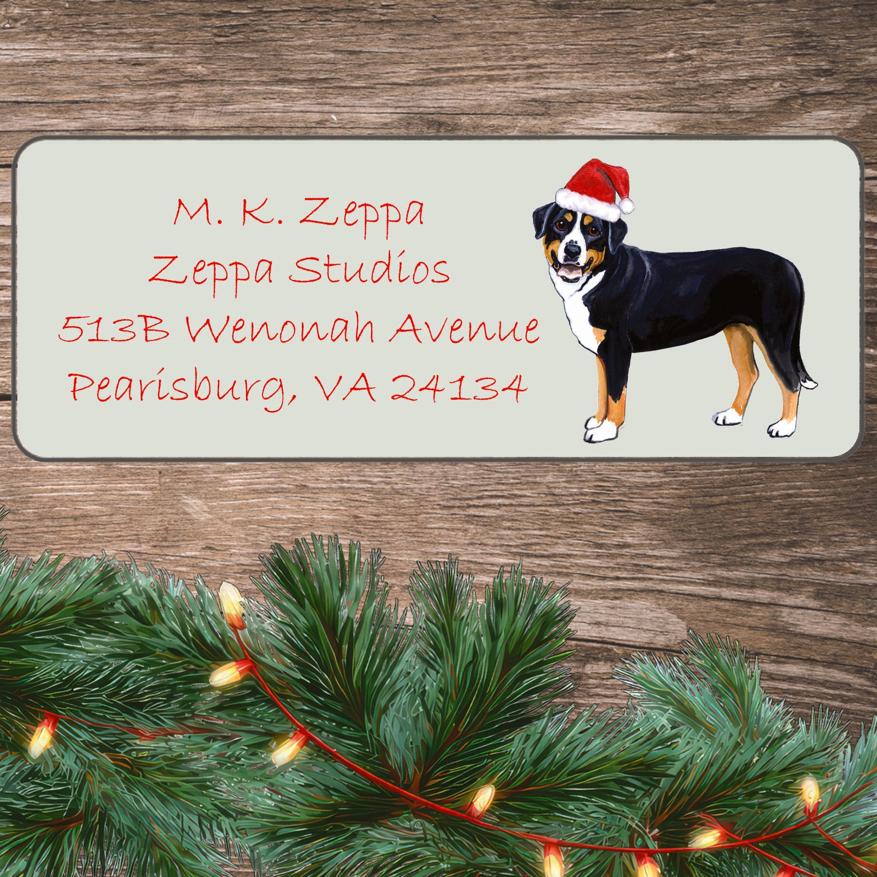 An illustration of a Greater Swiss Mountain Dog  wearing a Santa Hat on an ivory return address label set off by a wood surface with holiday greenery background.