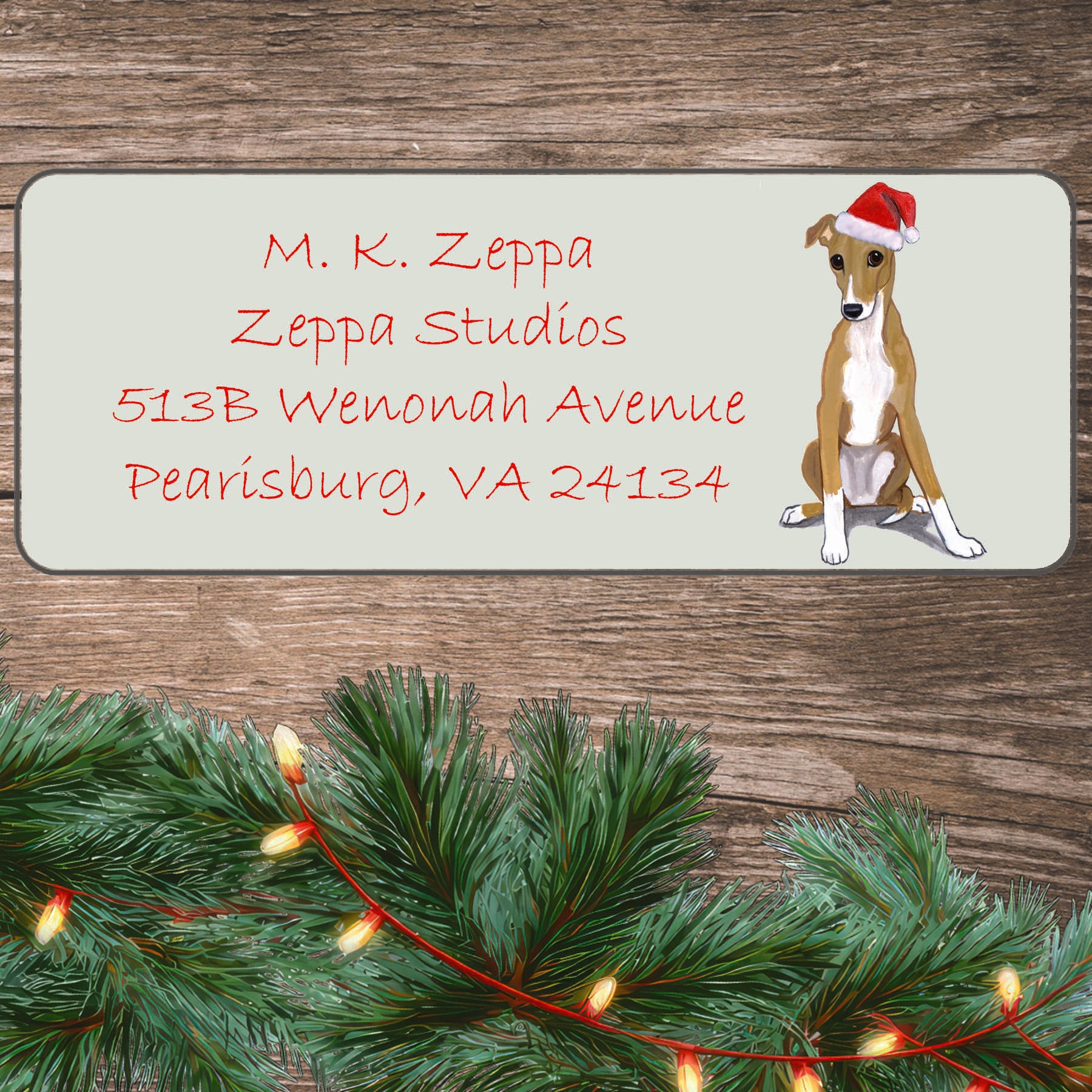 An illustration of a Greyhound puppy wearing a Santa Hat on an ivory return address label set off by a wood surface with holiday greenery background.