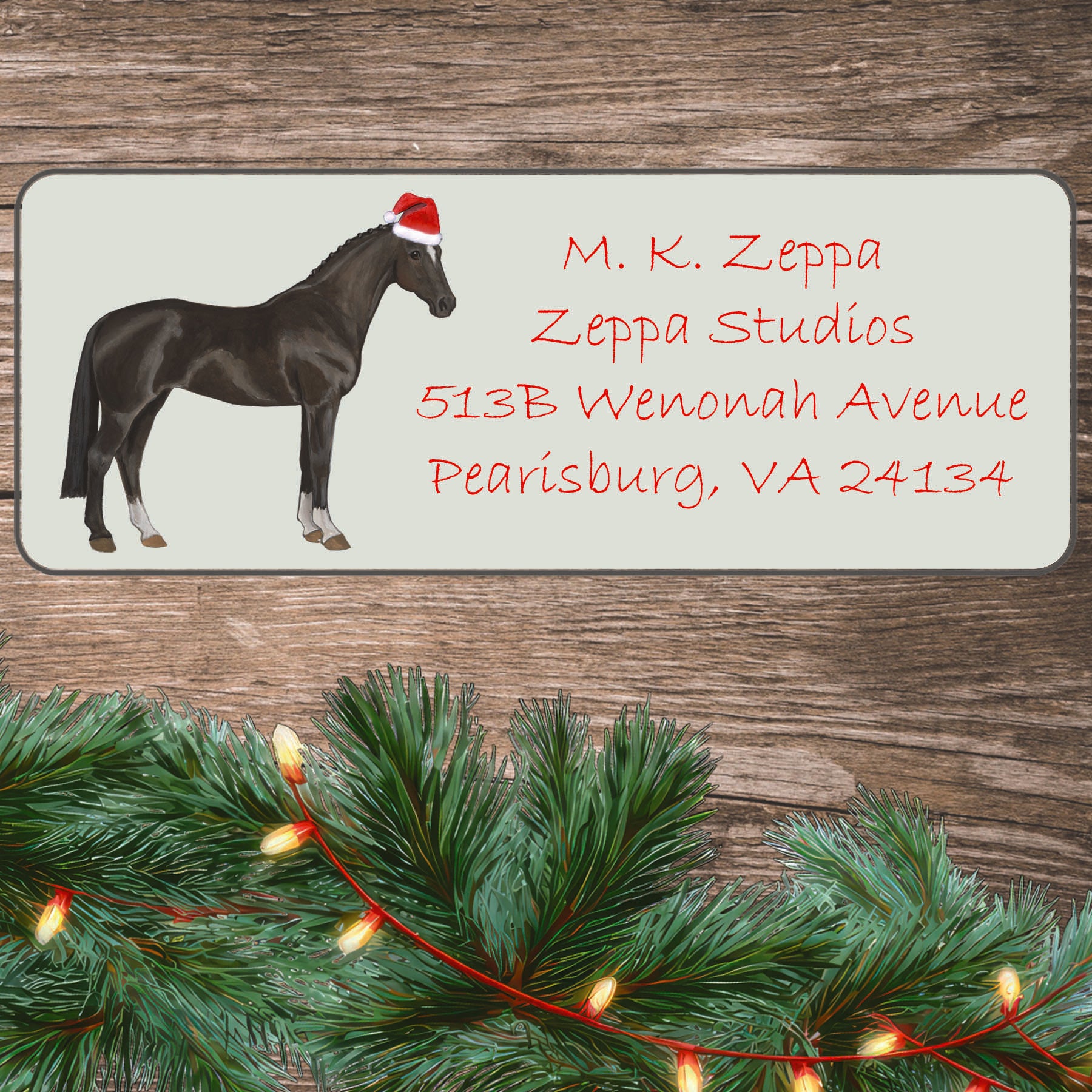An illustration of a Hanoverian horse wearing a Santa Hat on an ivory return address label set off by a wood surface with holiday greenery background.