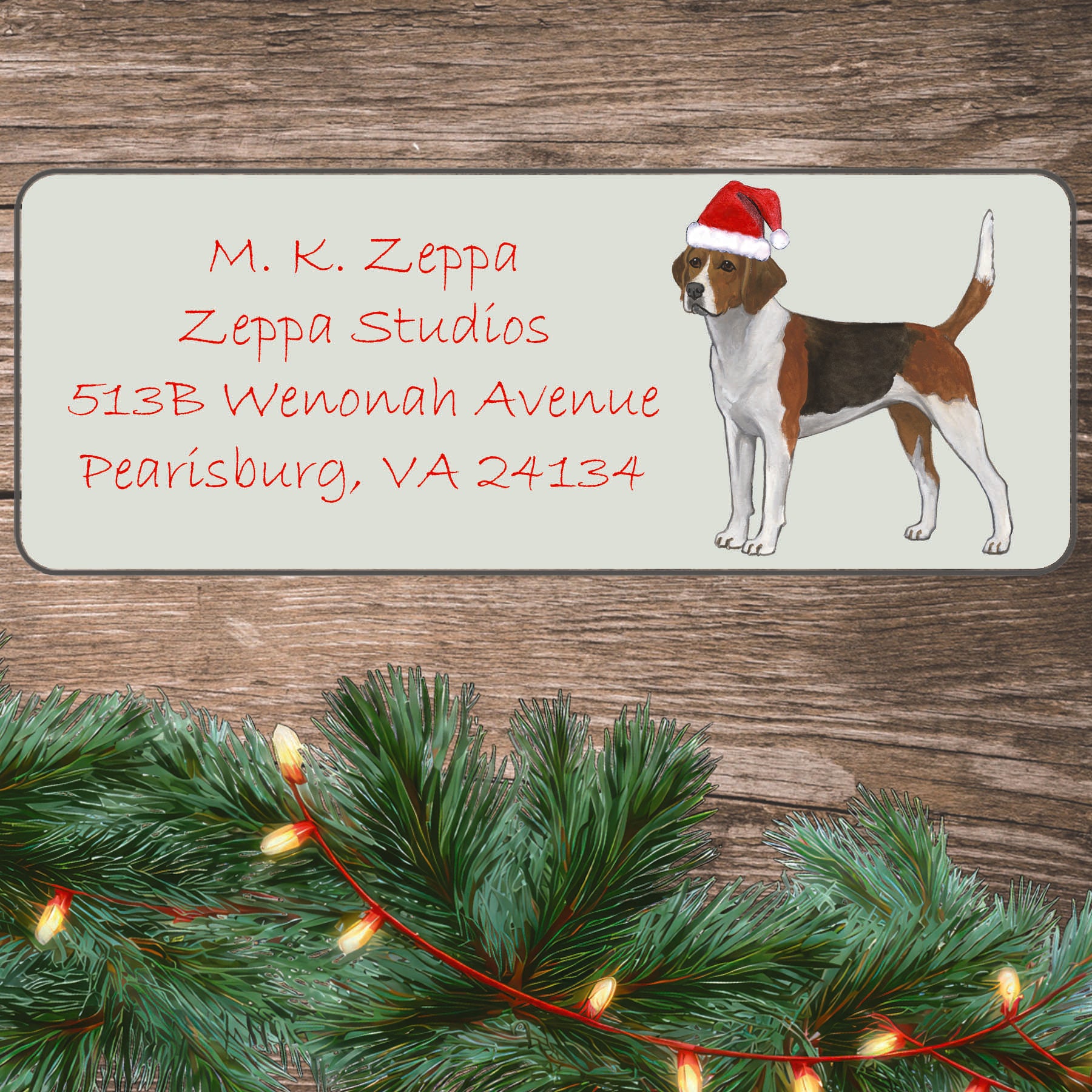 A Harrier in a Santa Hat illustration on an ivory return address label set off by a wood surface with holiday greenery background.