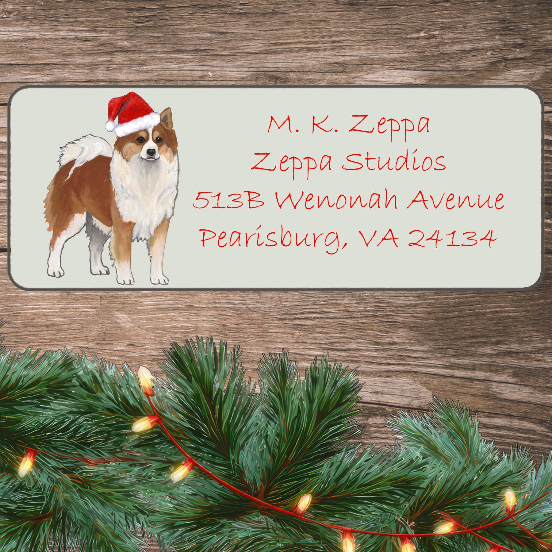 An illustration of an Icelandic Sheepdog wearing a Santa Hat on an ivory return address label set off by a wood surface with holiday greenery background.