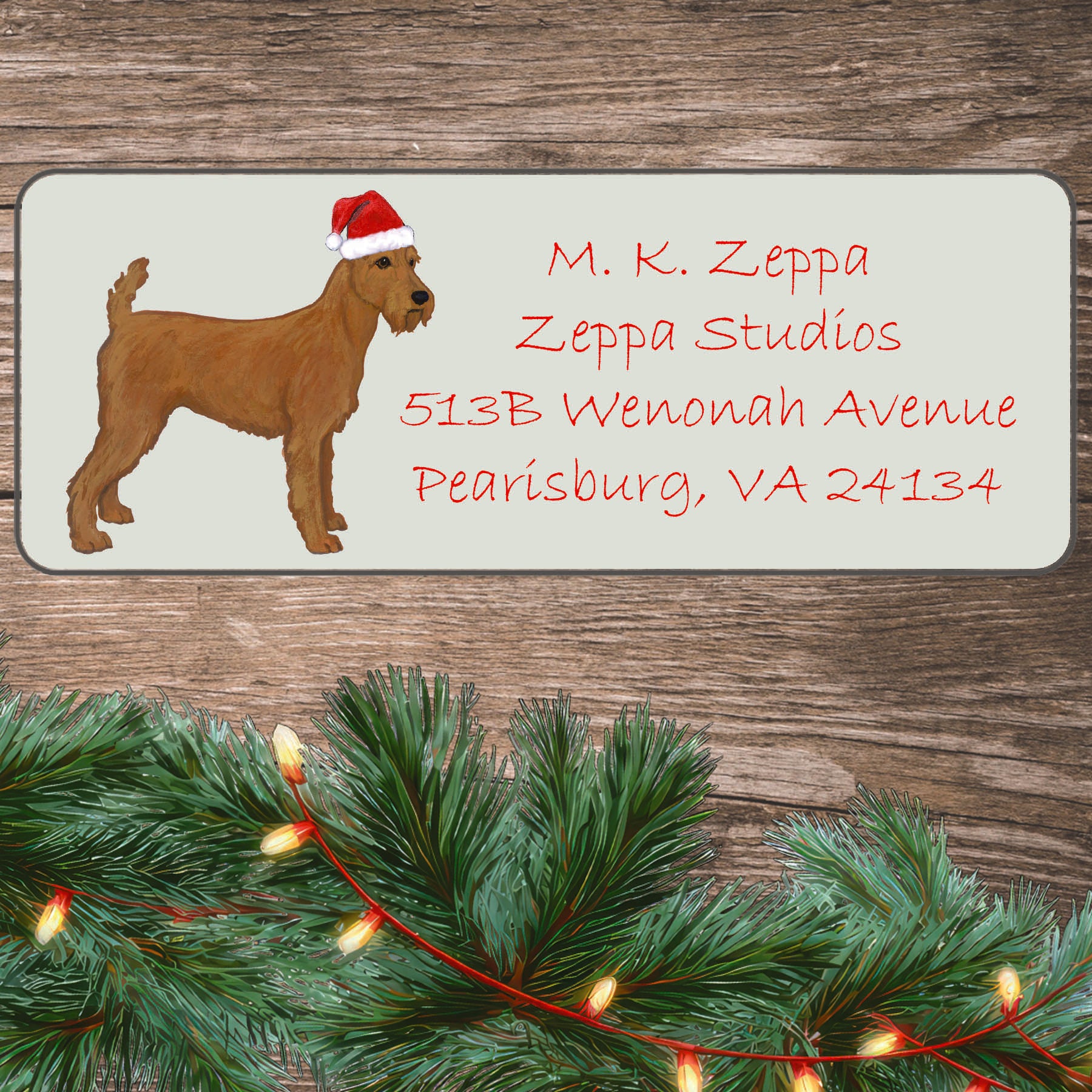 An illustration of an Irish Terrier  wearing a Santa Hat on an ivory return address label set off by a wood surface with holiday greenery background.