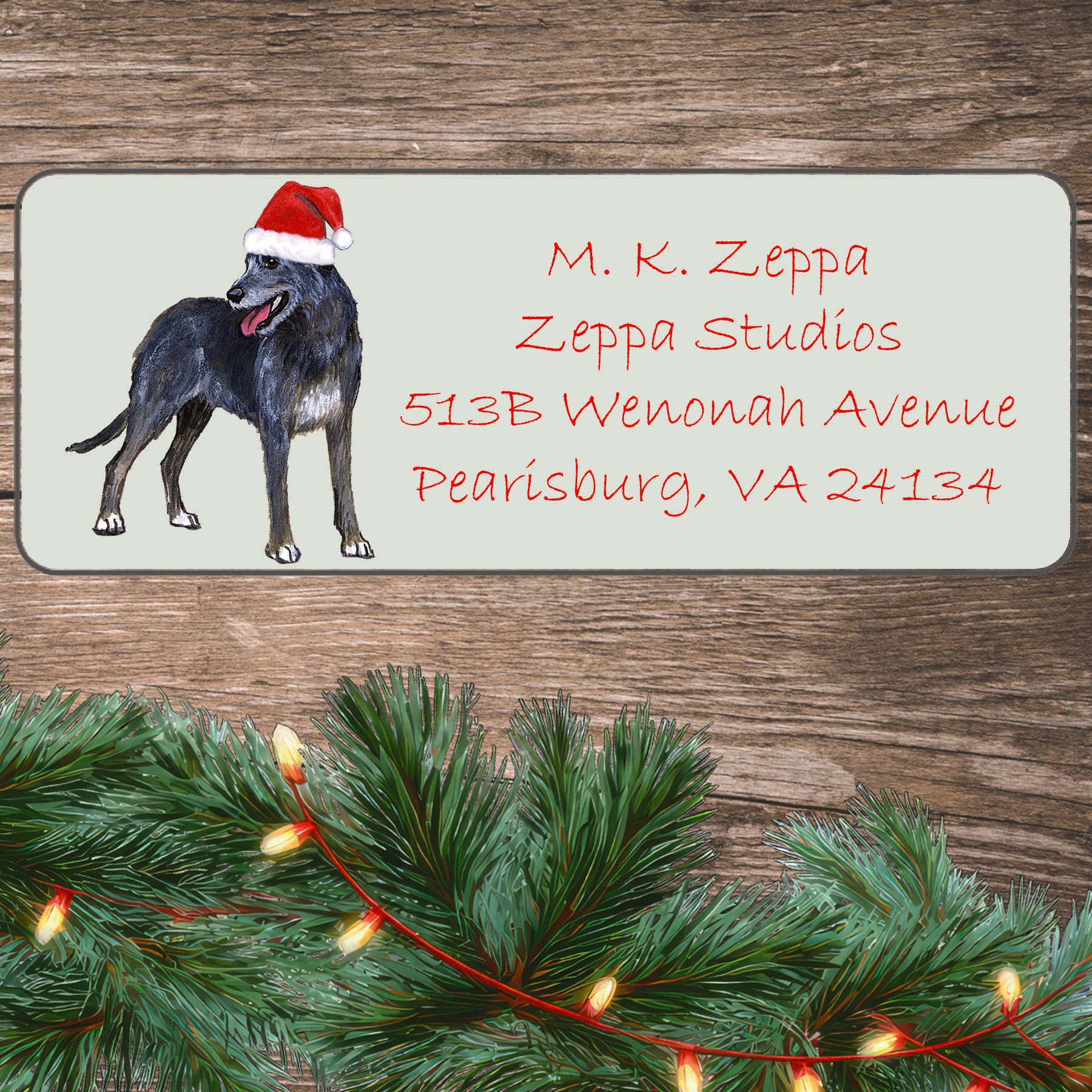 An illustration of an Irish Wolfhound  wearing a Santa Hat on an ivory return address label set off by a wood surface with holiday greenery background.