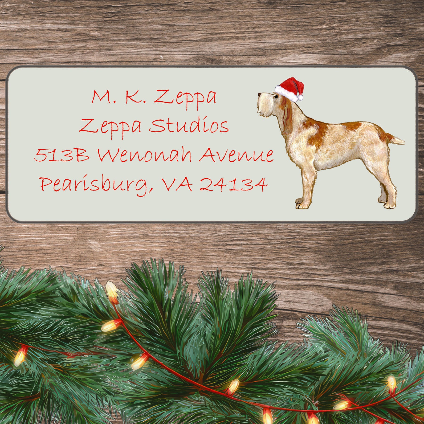 An illustration of a red and white Italian Spinone wearing a Santa Hat on an ivory return address label set off by a wood surface with holiday greenery background.