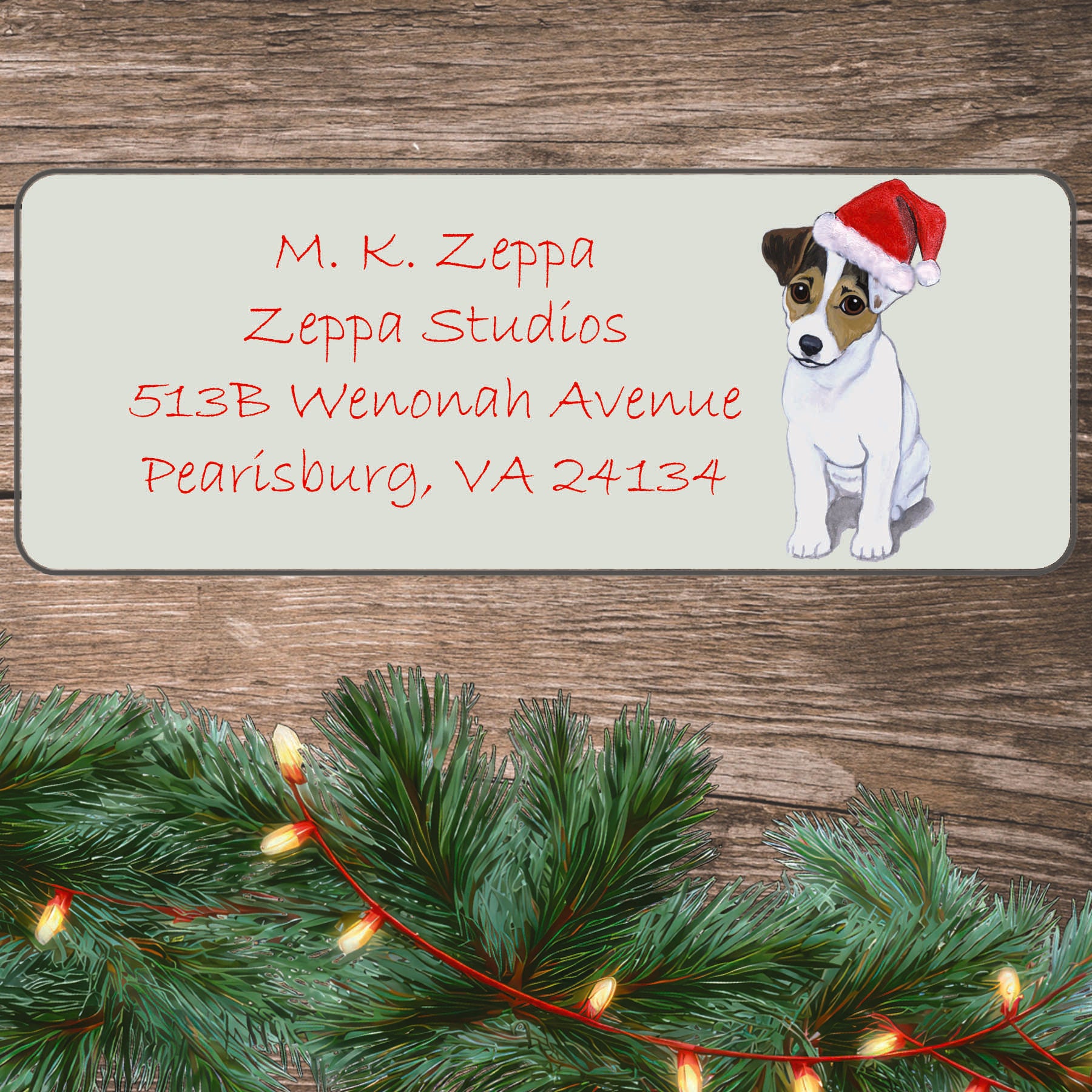 An illustration of a Jack Russell puppy wearing a Santa Hat on an ivory return address label set off by a wood surface with holiday greenery background.