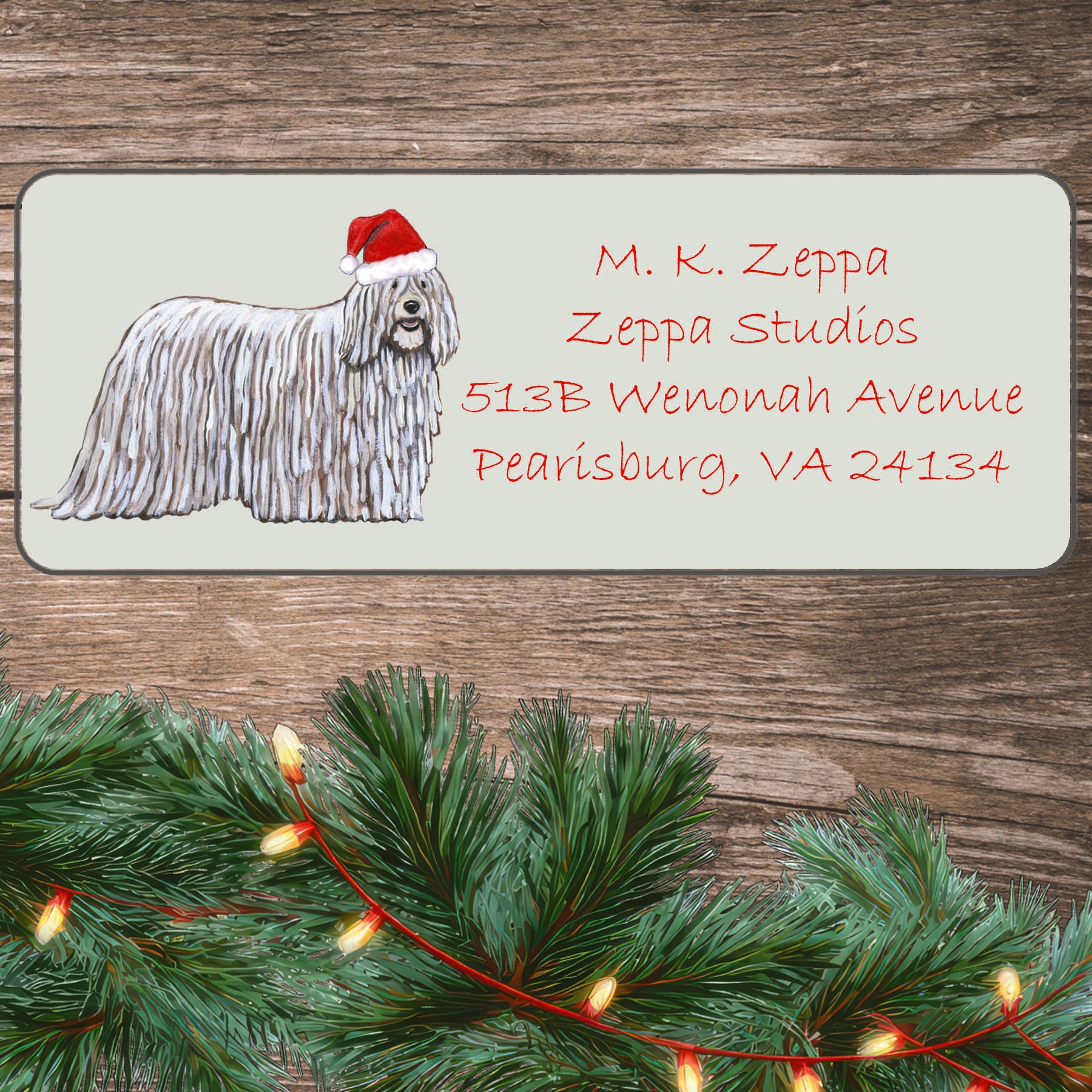 An illustration of a Komondor wearing a Santa Hat on an ivory return address label set off by a wood surface with holiday greenery background.