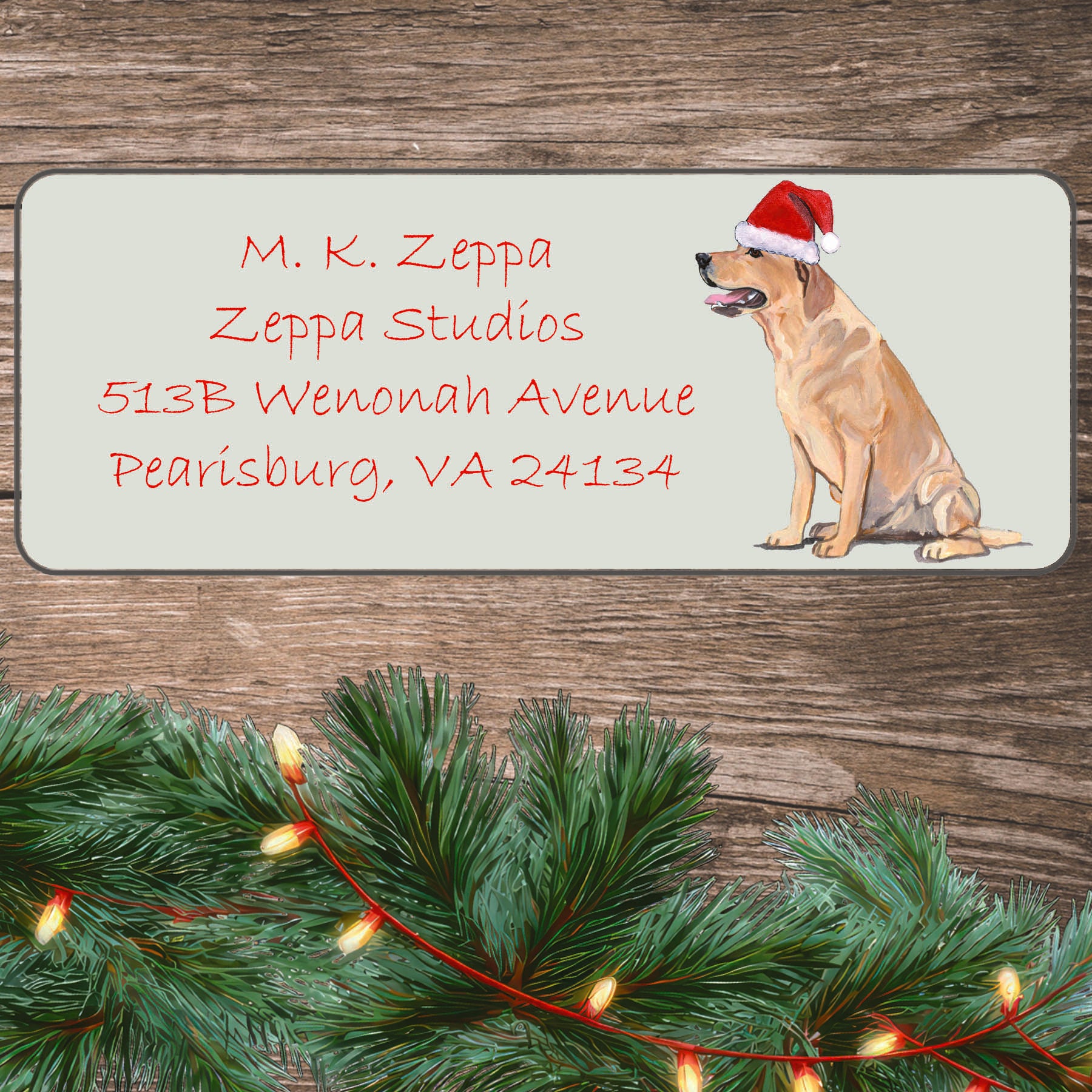 An illustration of a Yellow Lab  wearing a Santa Hat on an ivory return address label set off by a wood surface with holiday greenery background.