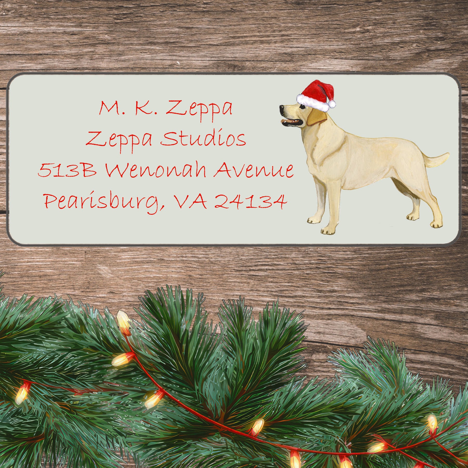 An illustration of a standing Yellow Lab wearing a Santa Hat on an ivory return address label set off by a wood surface with holiday greenery background.