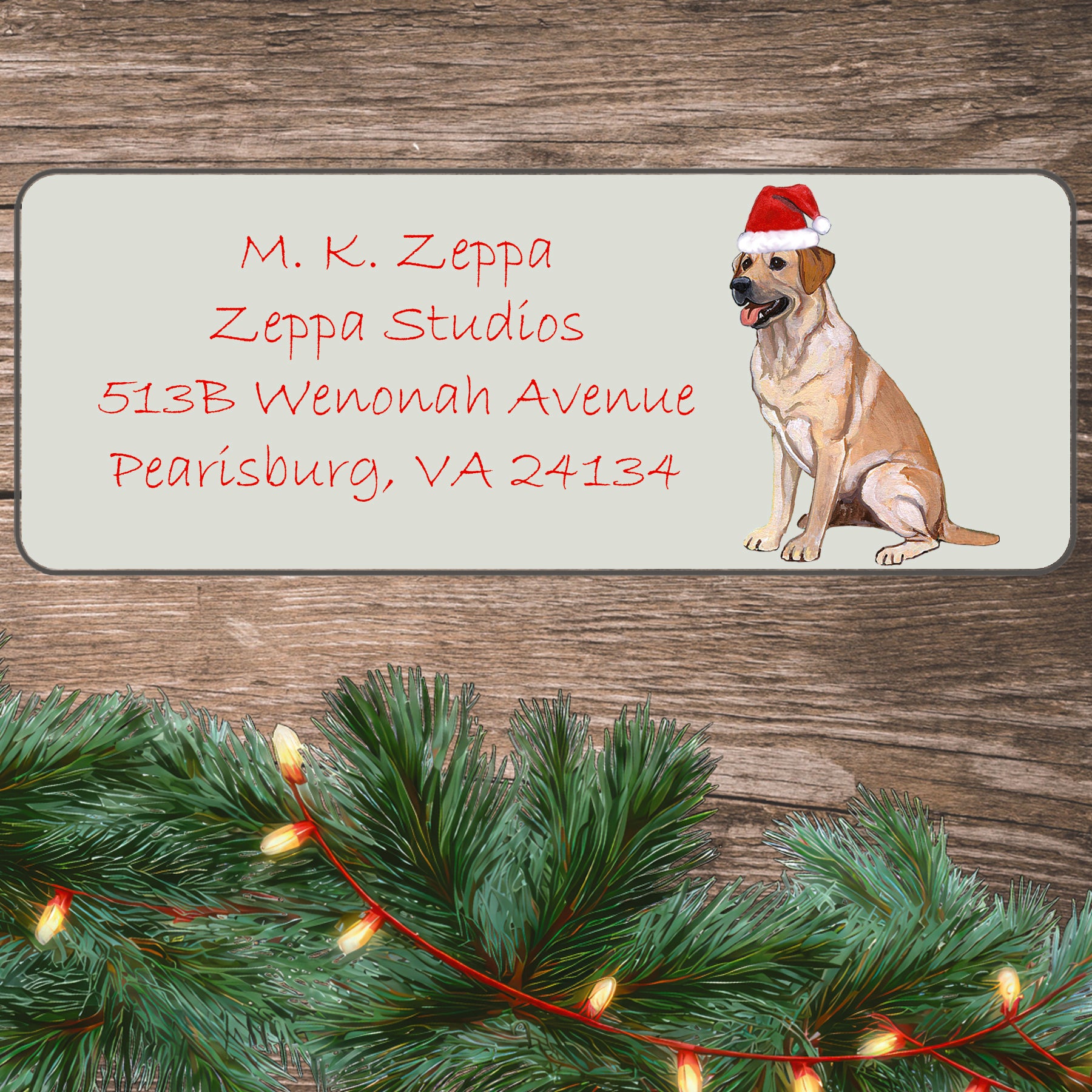 An illustration of a  Yellow Lab wearing a Santa Hat on an ivory return address label set off by a wood surface with holiday greenery background.