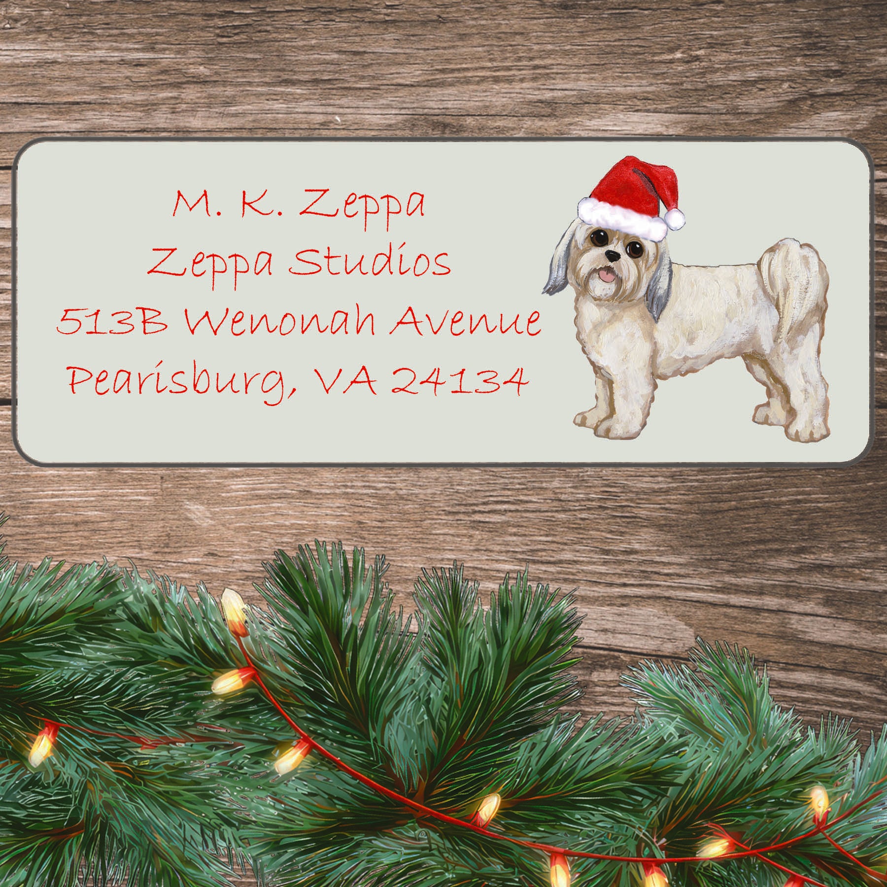 An illustration of a Lhasa Apso with a puppy clip wearing a Santa Hat on an ivory return address label set off by a wood surface with holiday greenery background.