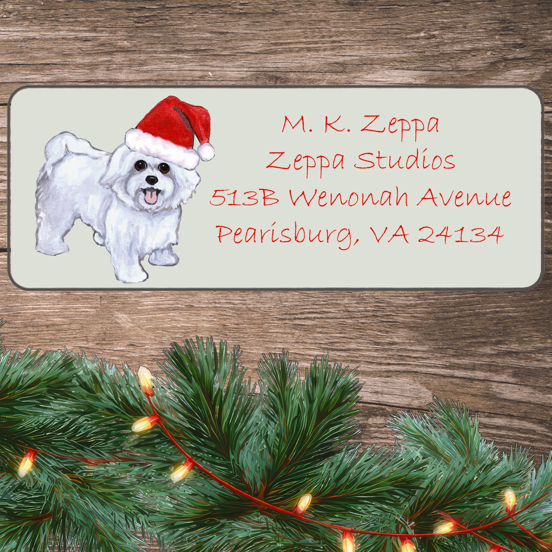 An illustration of a puppy clip Maltese wearing a Santa Hat on an ivory return address label set off by a wood surface with holiday greenery background.