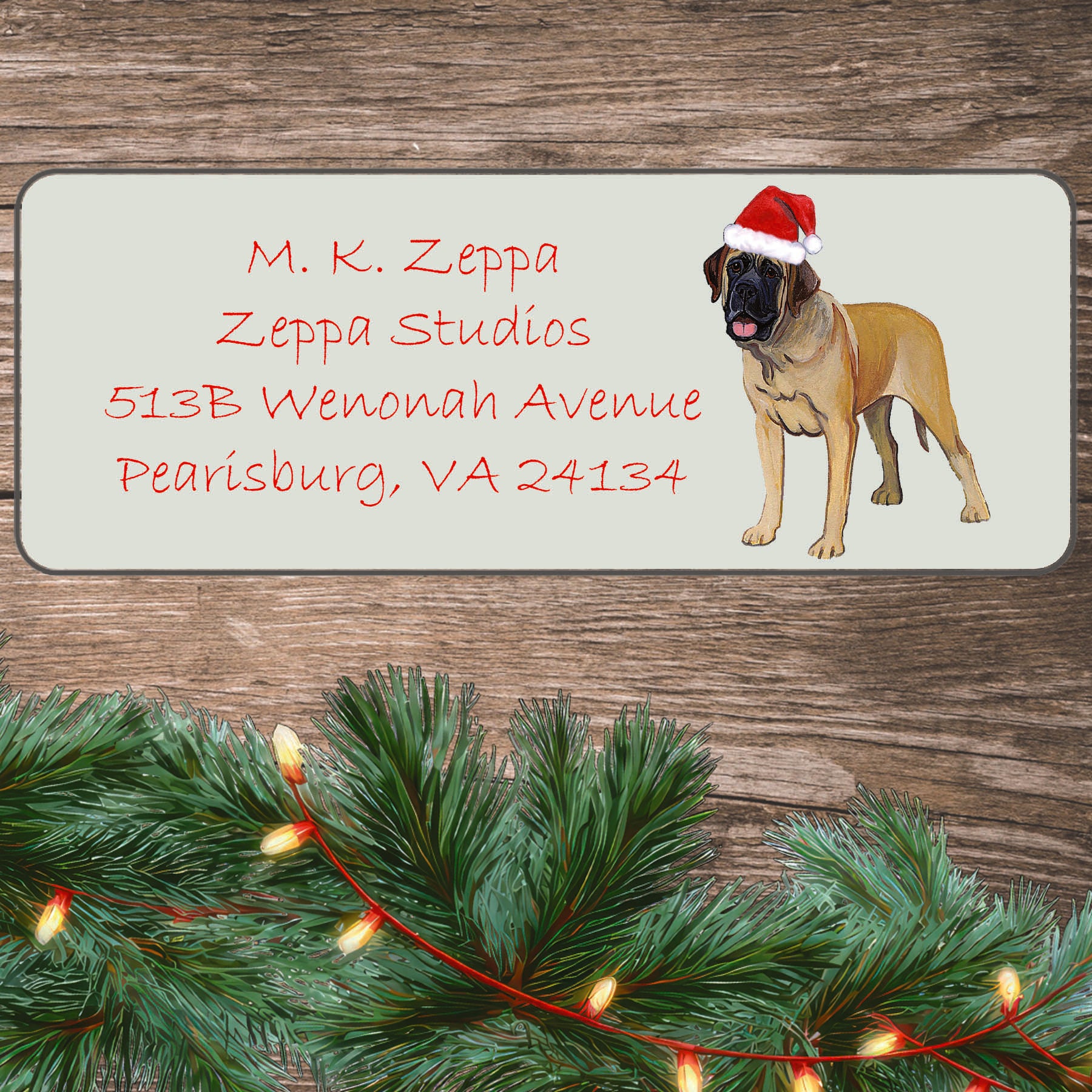 An illustration of a Mastiff wearing a Santa Hat on an ivory return address label set off by a wood surface with holiday greenery background.