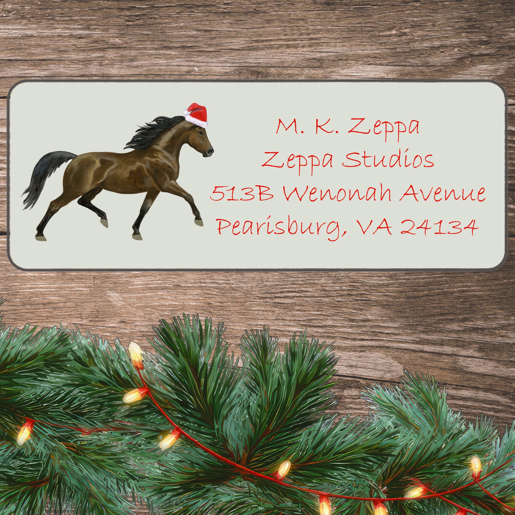 An illustration of a Morgan Horse wearing a Santa Hat on an ivory return address label set off by a wood surface with holiday greenery background.