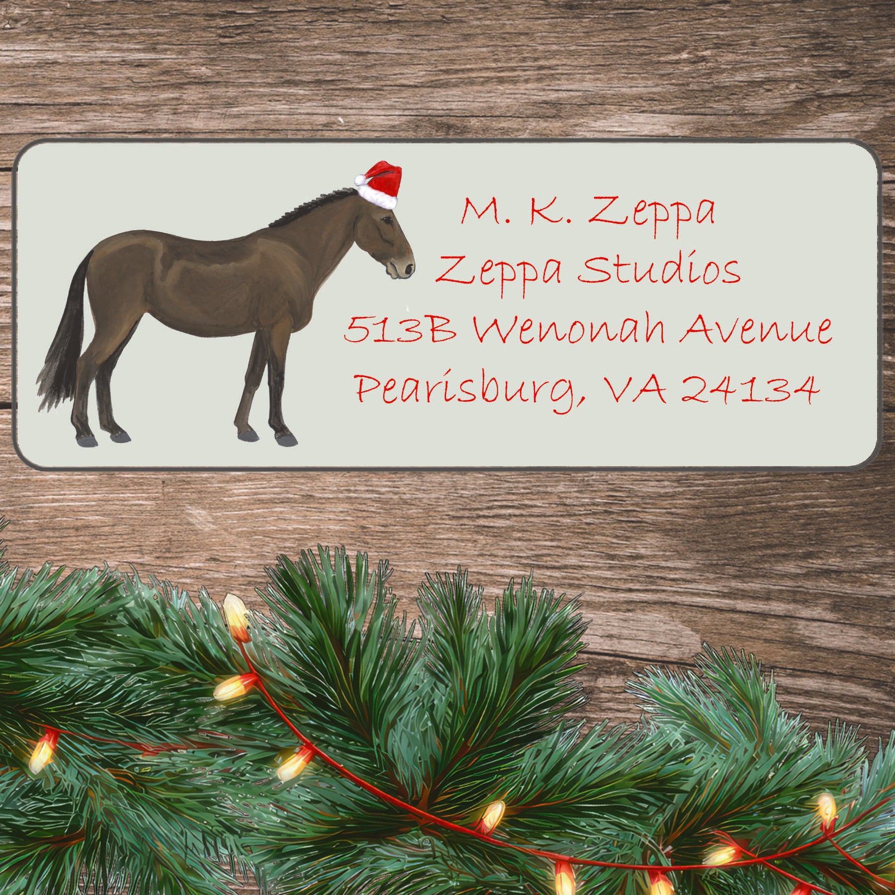 An illustration of a Mule wearing a Santa Hat on an ivory return address label set off by a wood surface with holiday greenery background.