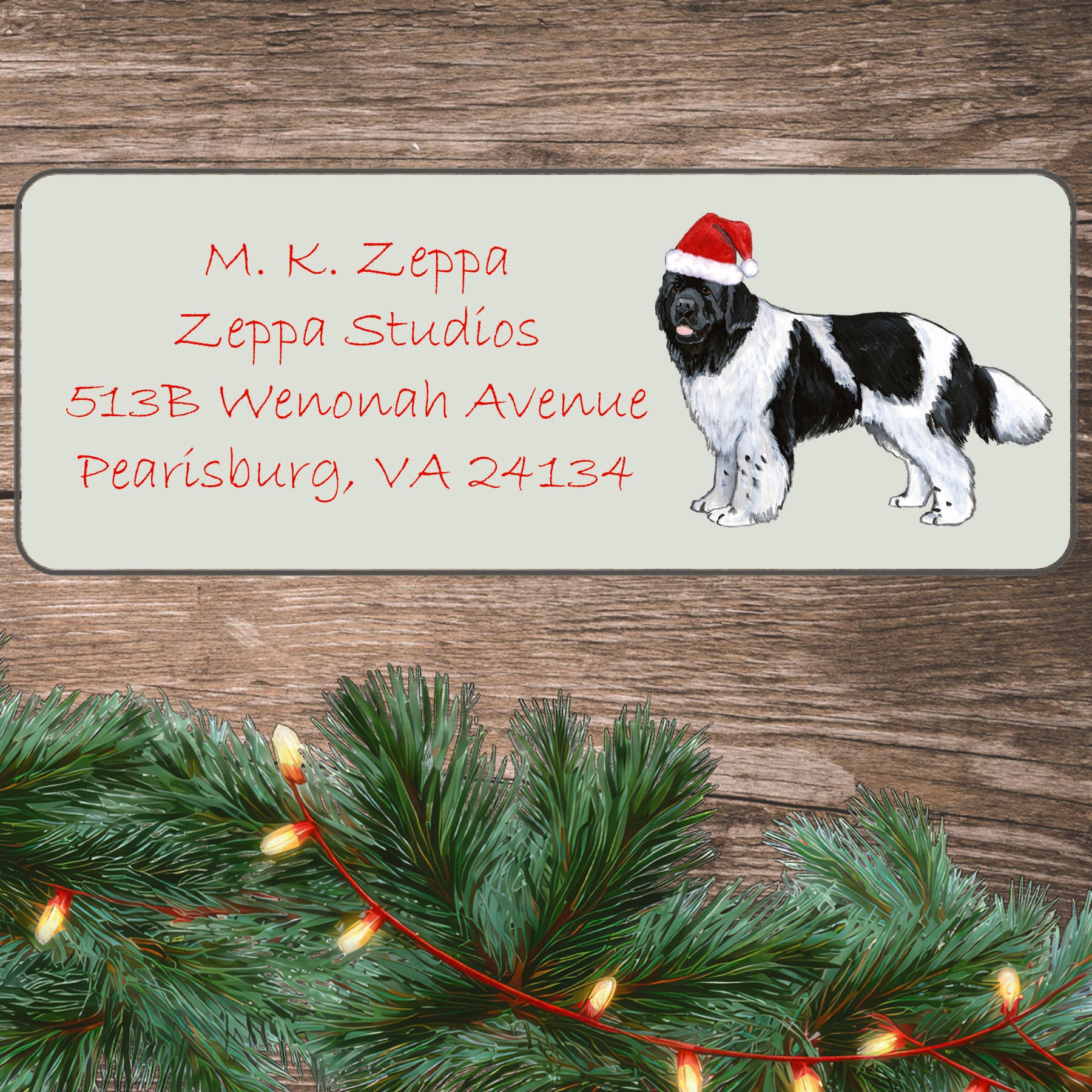An illustration of a Landseer Newfoundland wearing a Santa Hat on an ivory return address label set off by a wood surface with holiday greenery background.