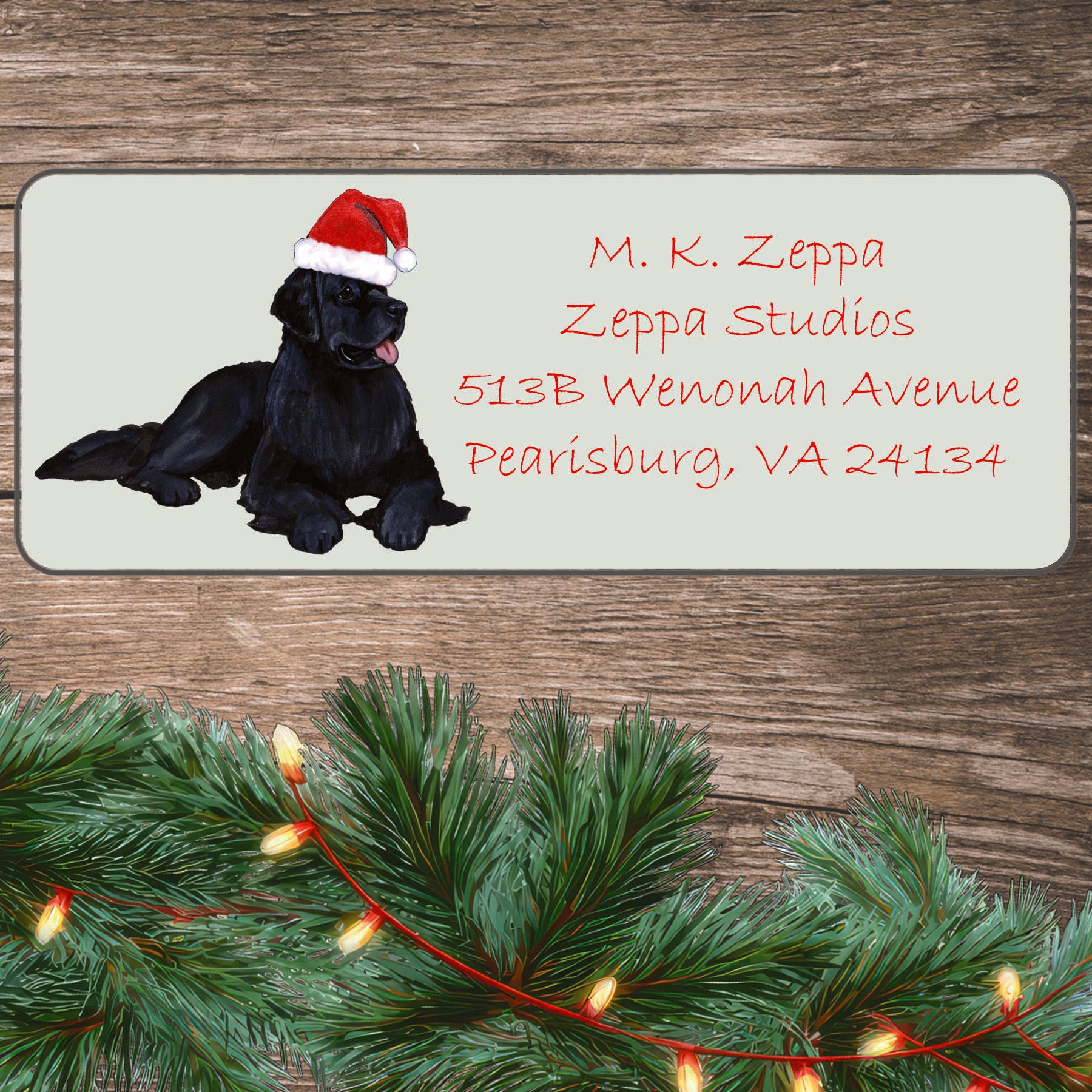 An illustration of a Newfoundland wearing a Santa Hat on an ivory return address label set off by a wood surface with holiday greenery background.
