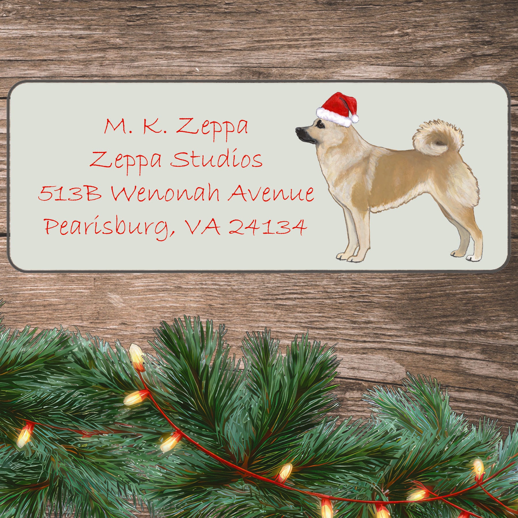 An illustration of a Norwegian Buhund wearing a Santa Hat on an ivory return address label set off by a wood surface with holiday greenery background.