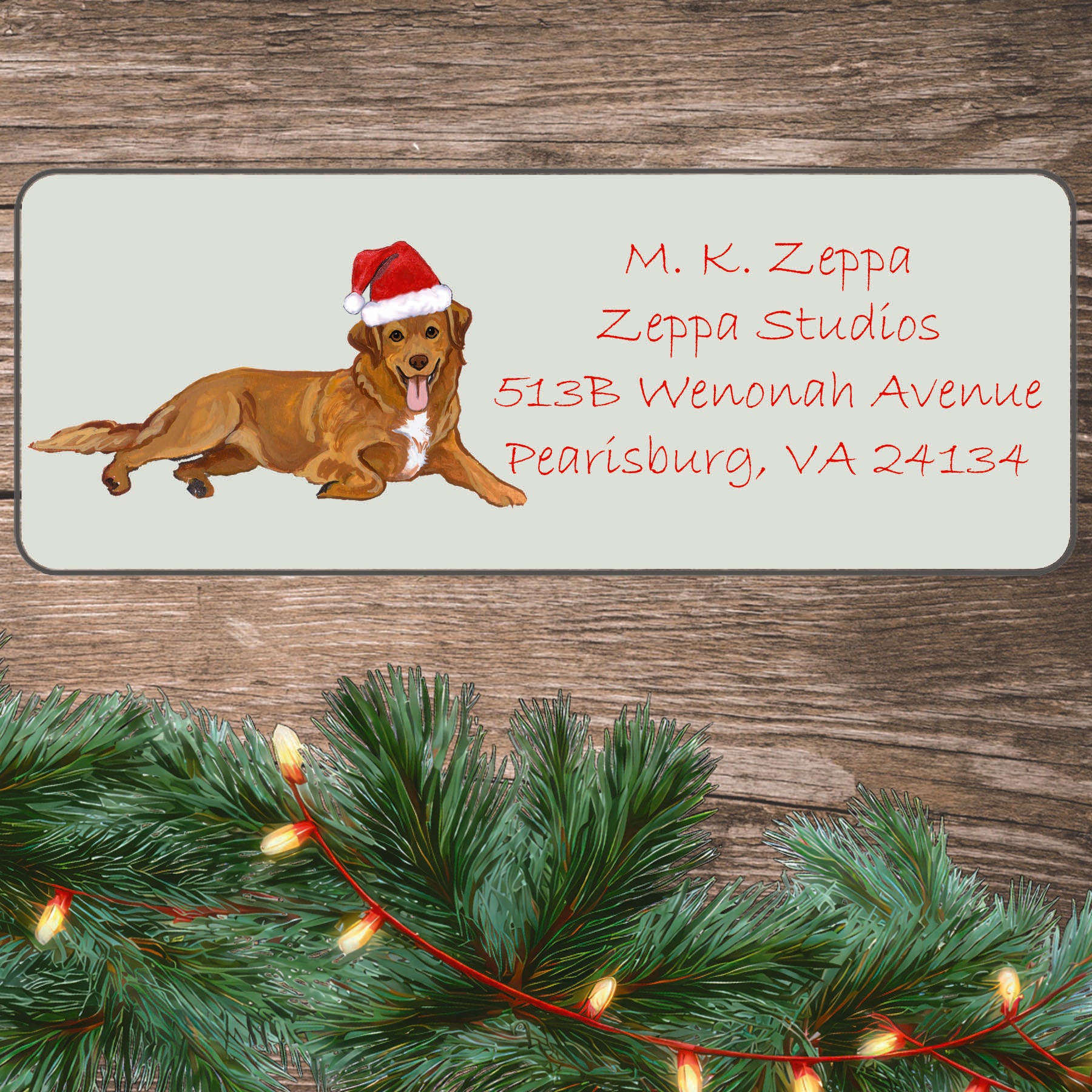 An illustration of a Nova Scotia Duck Tolling Retriever wearing a Santa Hat on an ivory return address label set off by a wood surface with holiday greenery background.