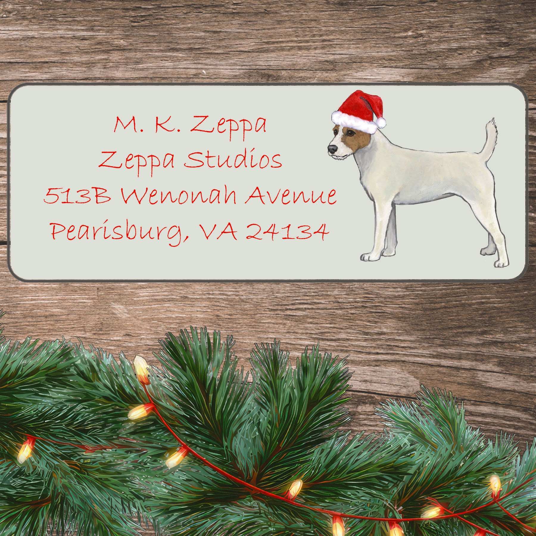 A Parson Russel Terrier in a Santa Hat illustration on an ivory return address label set off by a wood surface with holiday greenery background.
