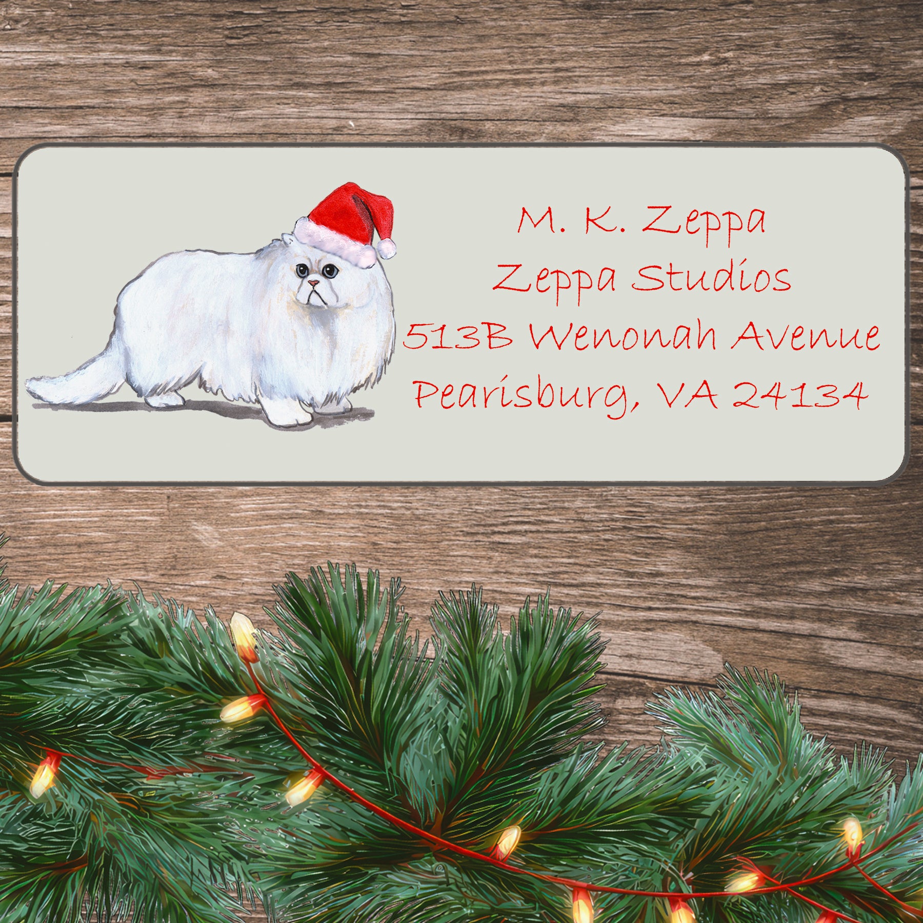 An illustration of a Persian Cat wearing a Santa Hat on an ivory return address label set off by a wood surface with holiday greenery background.