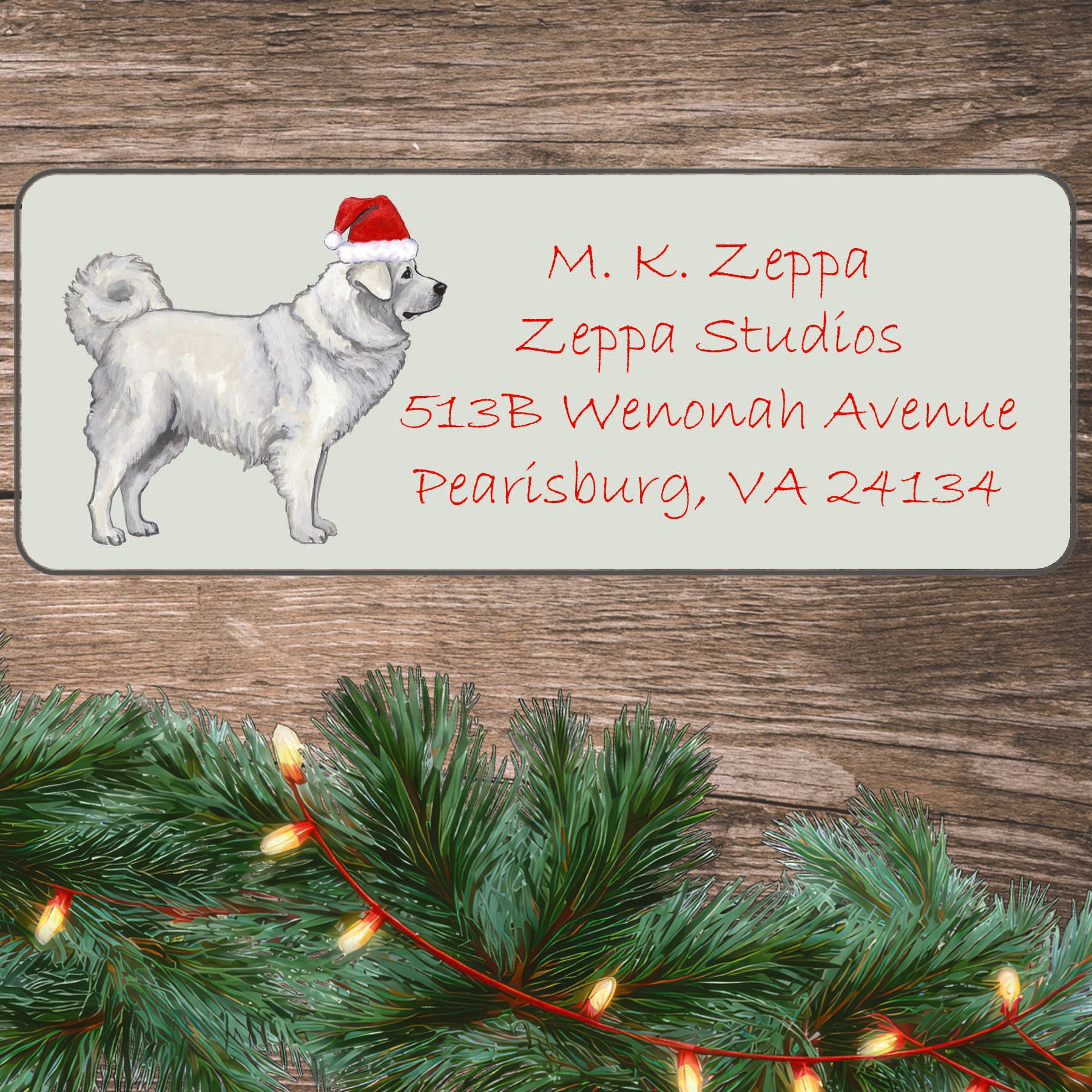 A Polish Tatra Sheepdog in a Santa Hat illustration on an ivory return address label set off by a wood surface with holiday greenery background.
