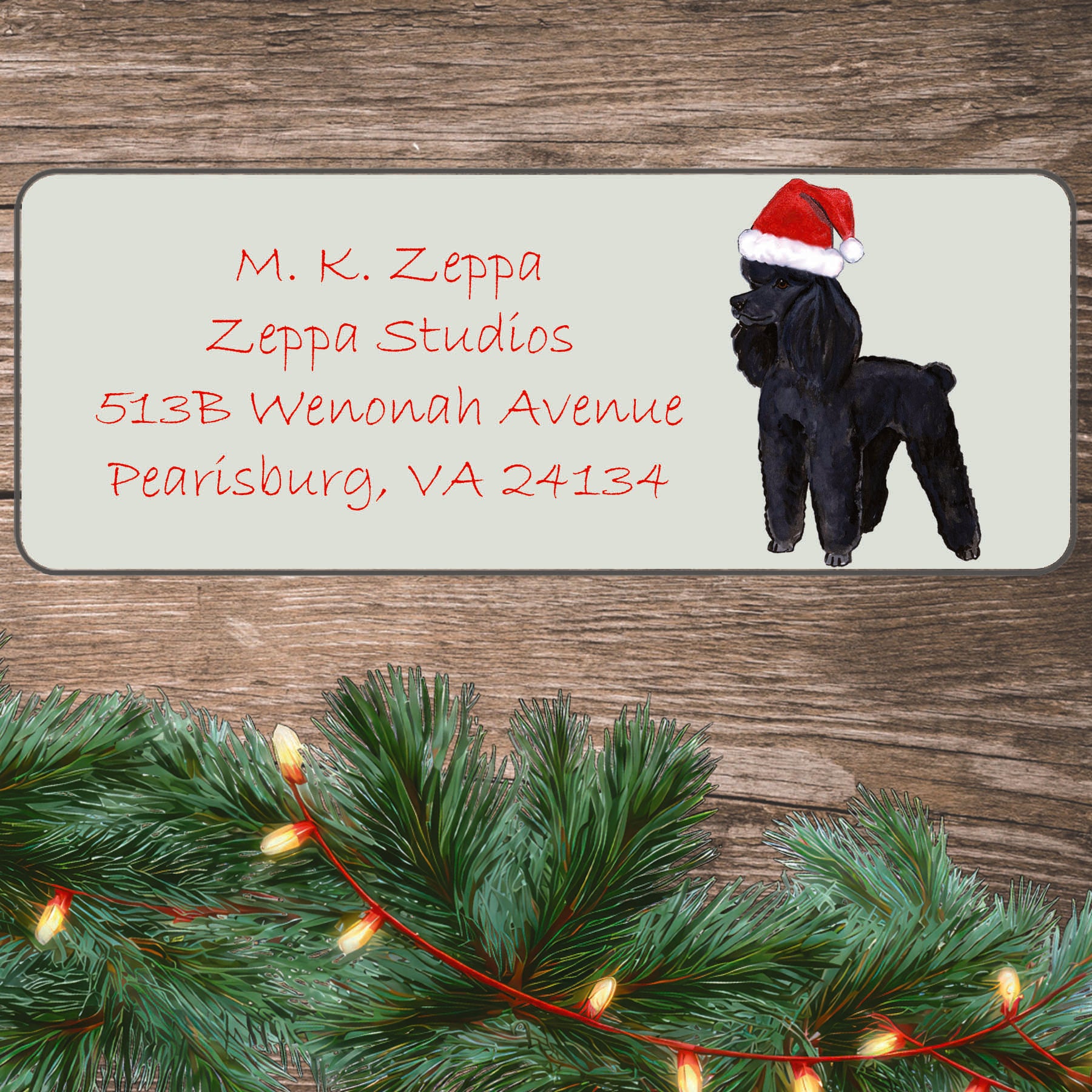 An illustration of a black Poodle wearing a Santa Hat on an ivory return address label set off by a wood surface with holiday greenery background.