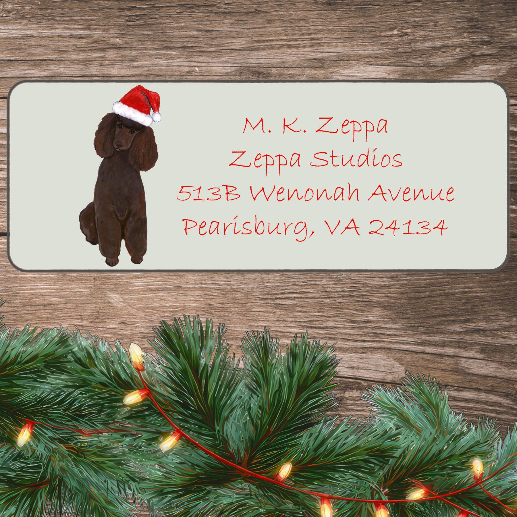 An illustration of a chocolate Poodle wearing a Santa Hat on an ivory return address label set off by a wood surface with holiday greenery background.