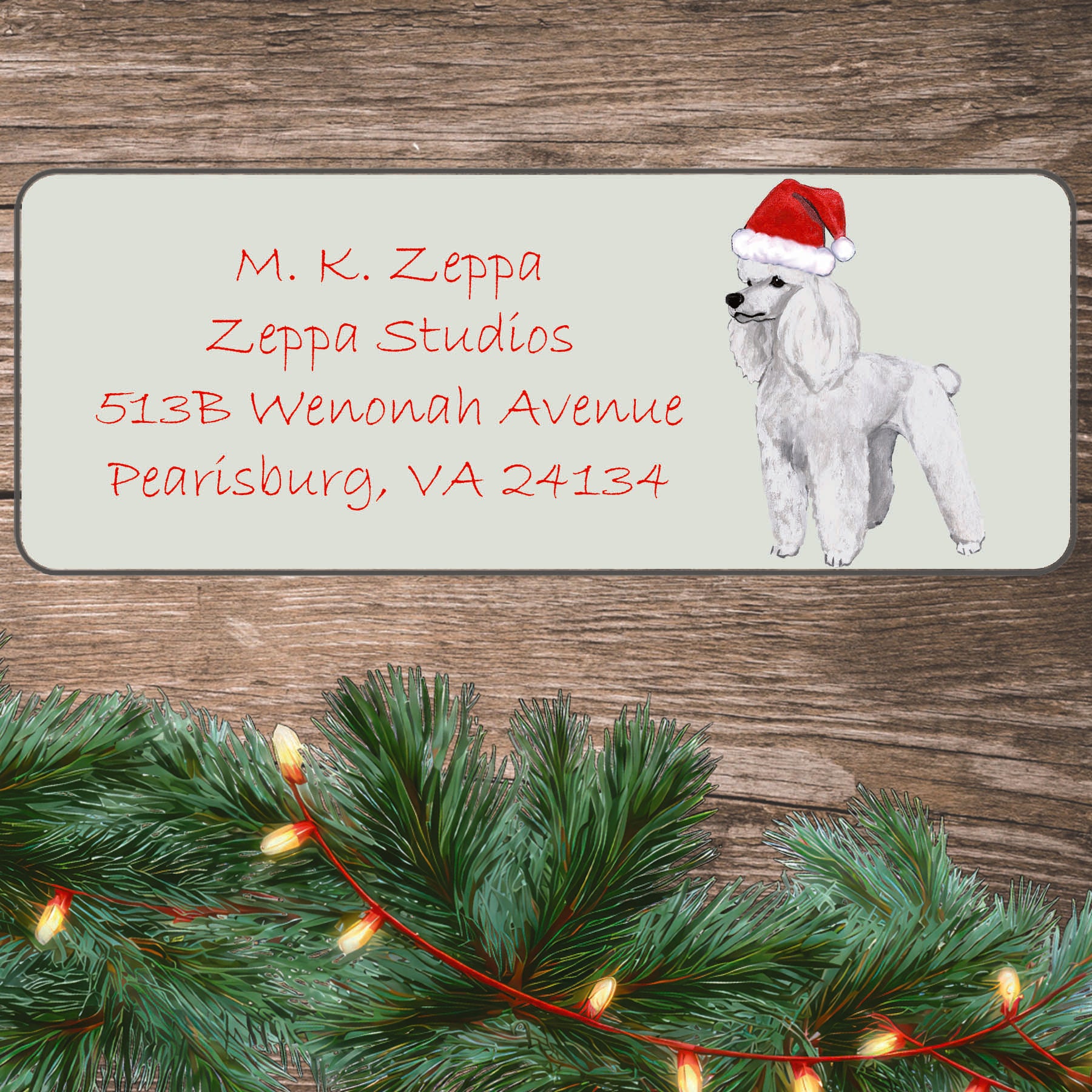 An illustration of a white Poodle wearing a Santa Hat on an ivory return address label set off by a wood surface with holiday greenery background.