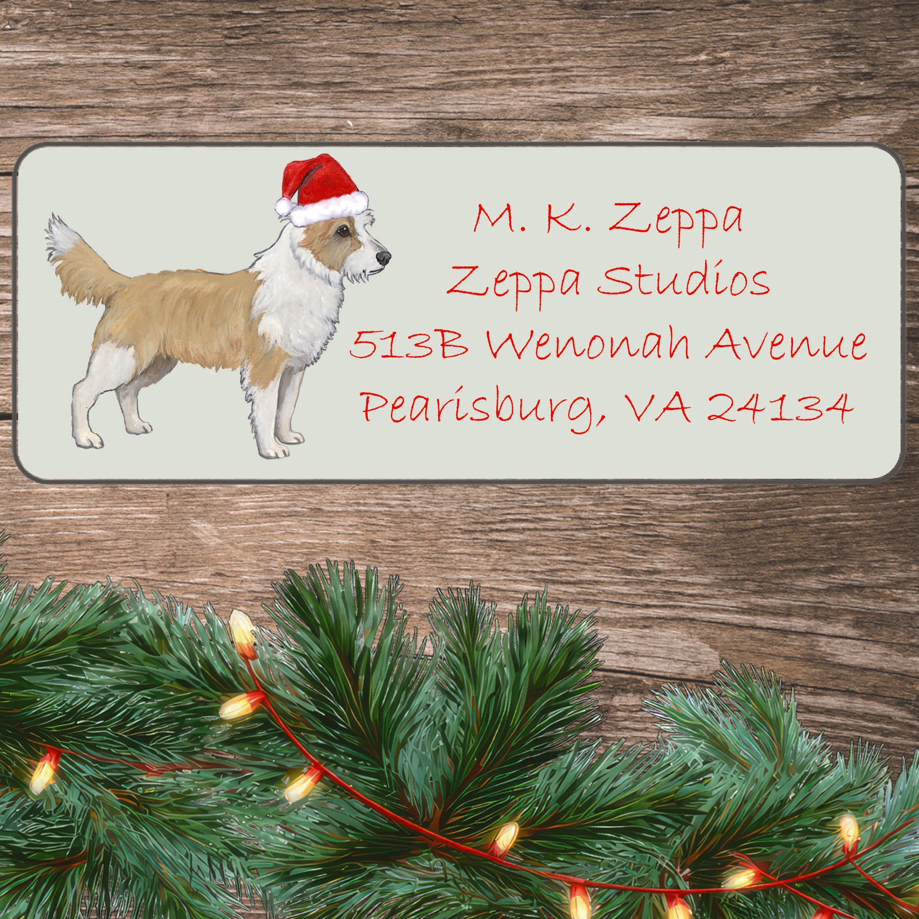 A Portuguese Podengo Pequeno in a Santa Hat illustration on an ivory return address label set off by a wood surface with holiday greenery background.
