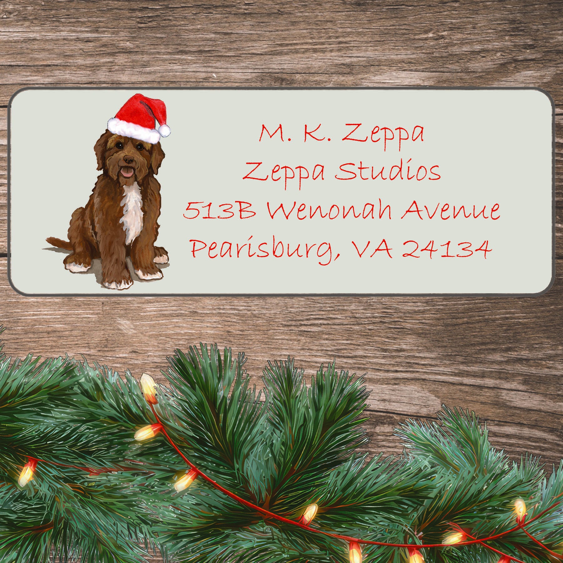 An illustration of a brown Portuguese  Water Dog wearing a Santa Hat on an ivory return address label set off by a wood surface with holiday greenery background.