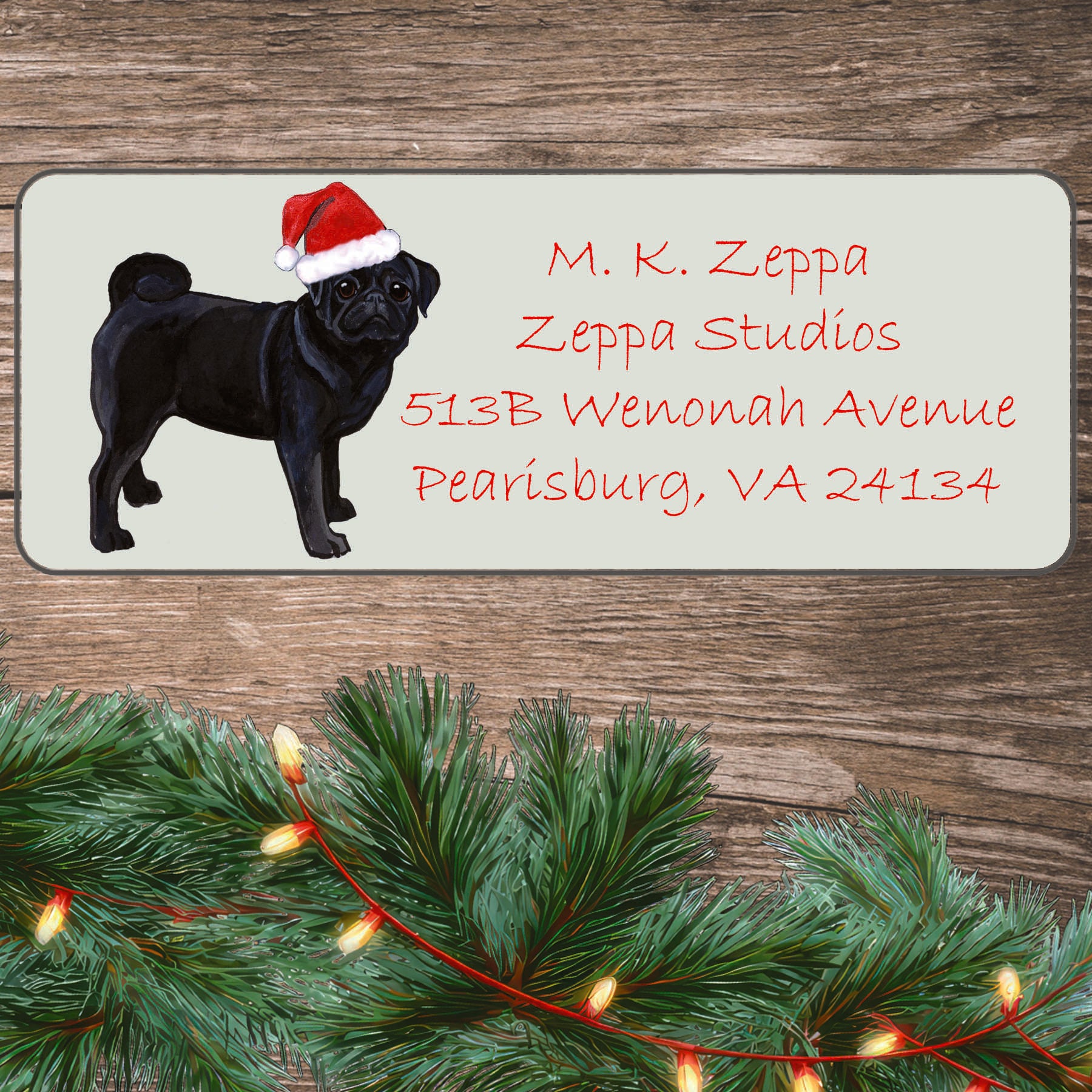 An illustration of a Black Pug wearing a Santa Hat on an ivory return address label set off by a wood surface with holiday greenery background.