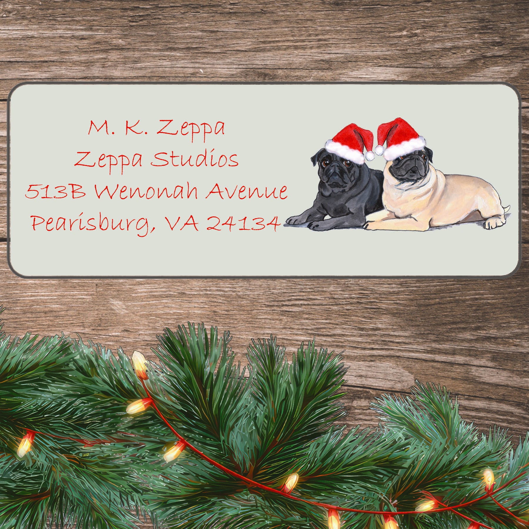 An illustration of a Pug pair wearing a Santa Hat on an ivory return address label set off by a wood surface with holiday greenery background.