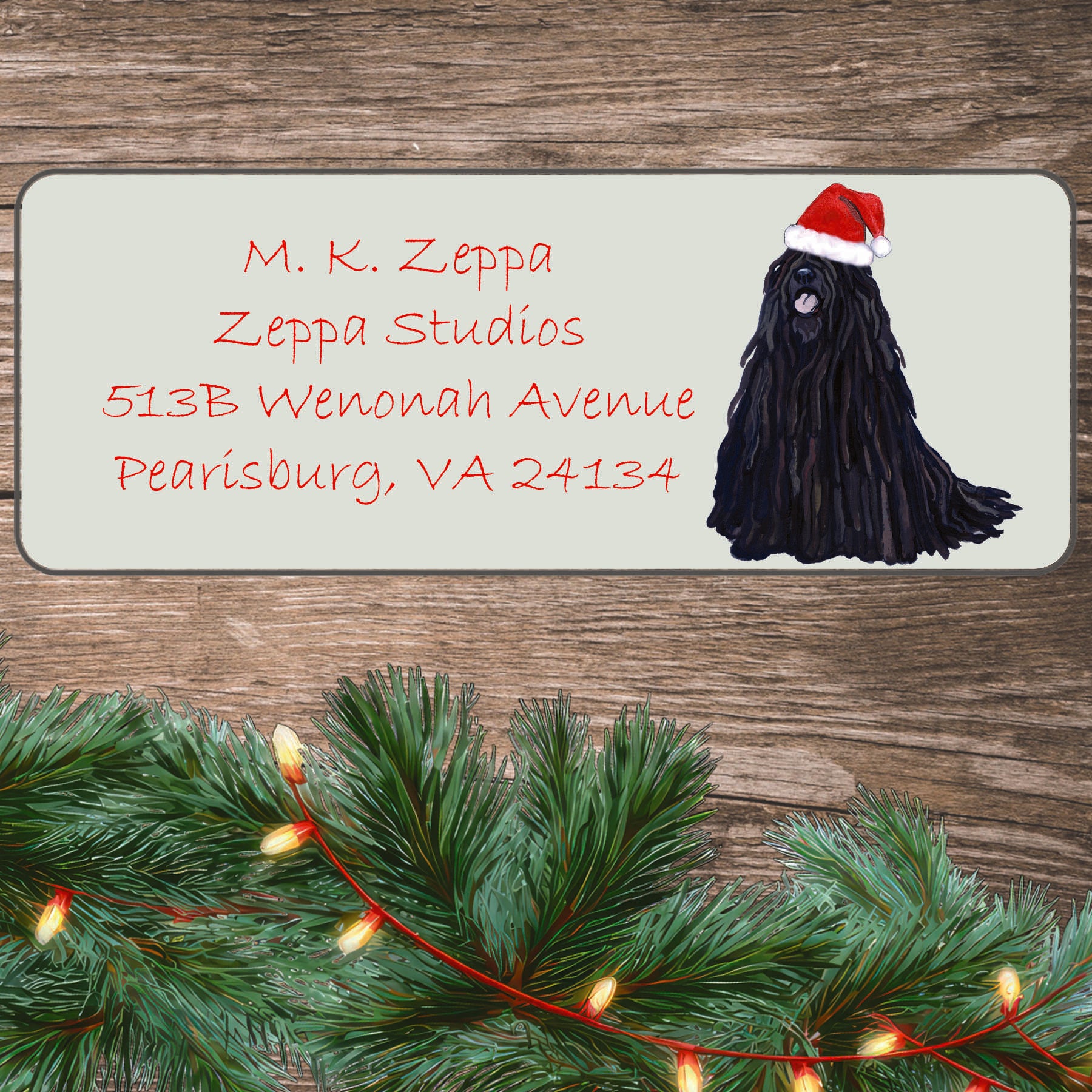 An illustration of a Puli wearing a Santa Hat on an ivory return address label set off by a wood surface with holiday greenery background.