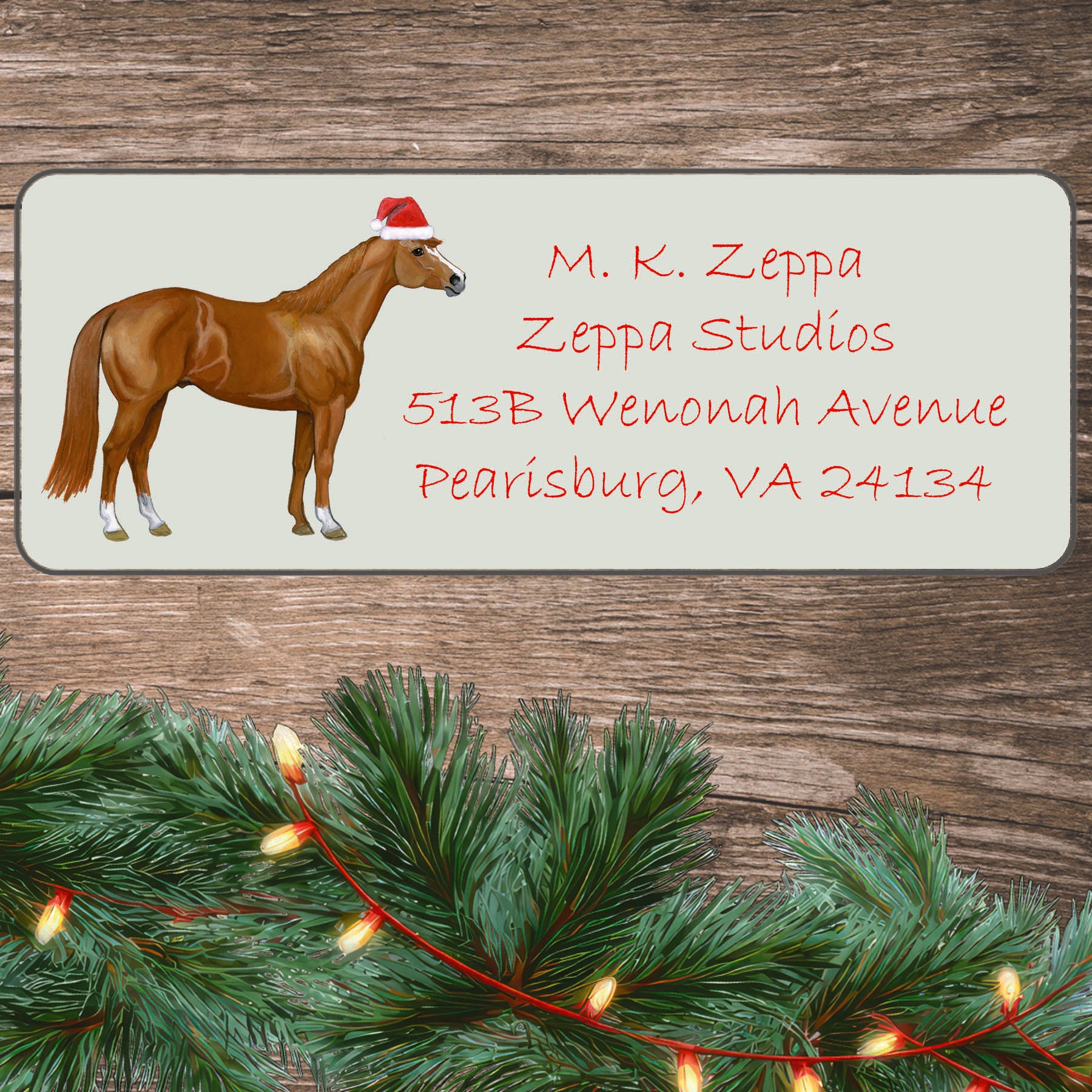 An illustration of a Quarter Horse wearing a Santa Hat on an ivory return address label set off by a wood surface with holiday greenery background.