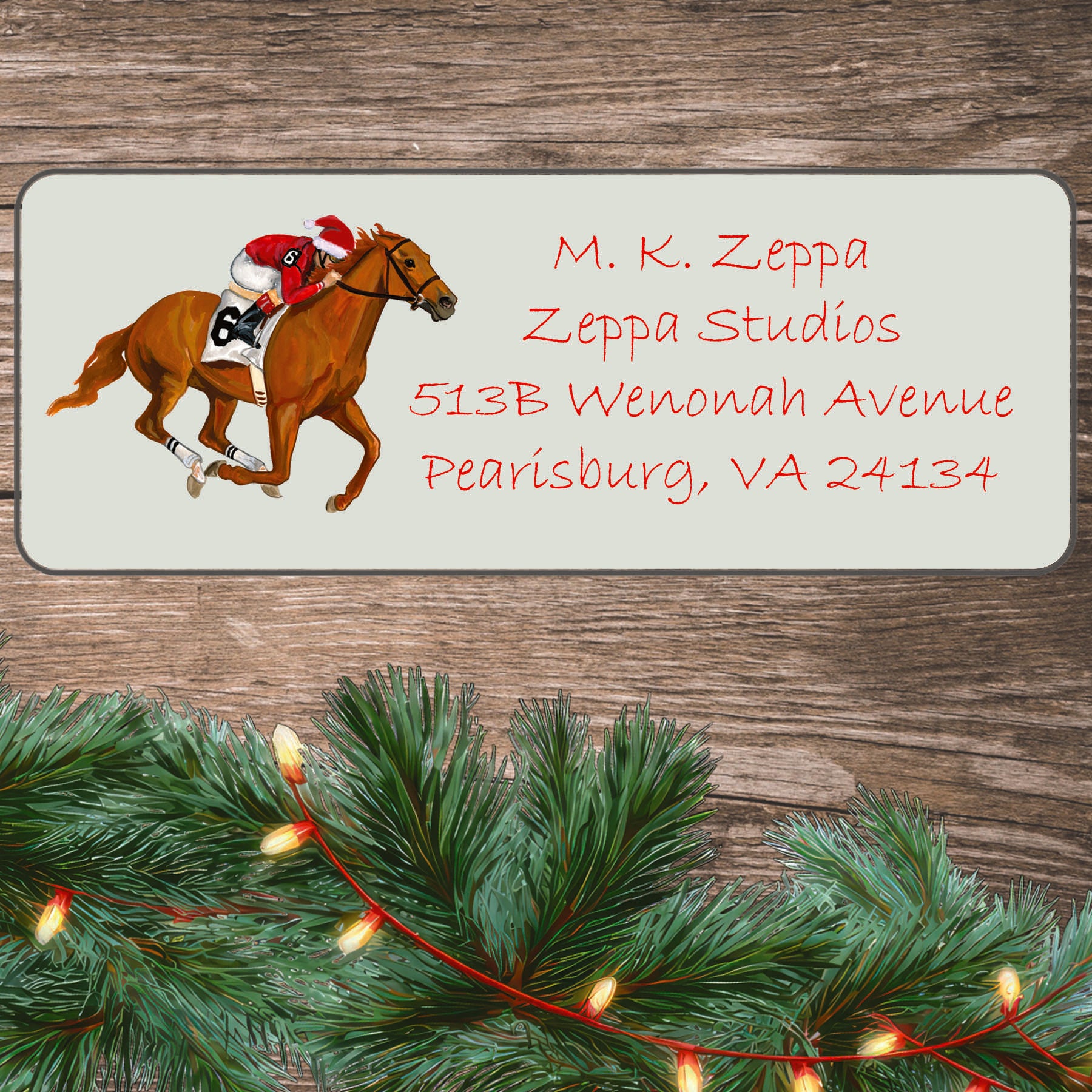 An illustration of a race horse galloping with a jockey wearing a Santa Hat on an ivory return address label set off by a wood surface with holiday greenery background.