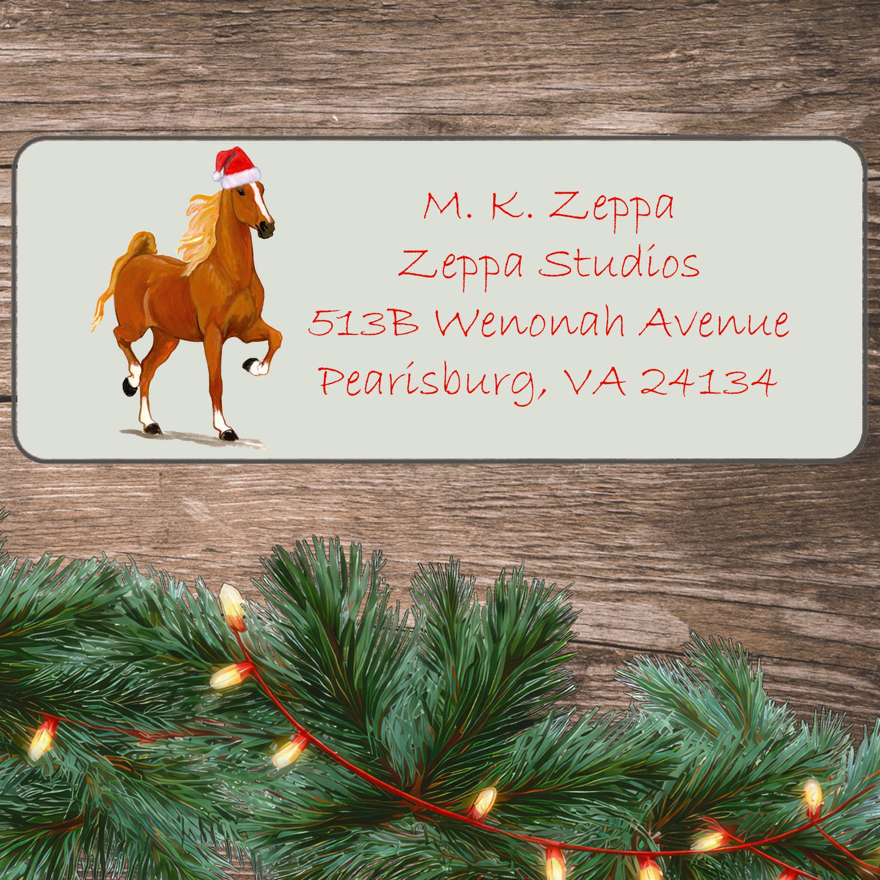 An illustration of a Saddlebred Horse wearing a Santa Hat on an ivory return address label set off by a wood surface with holiday greenery background.