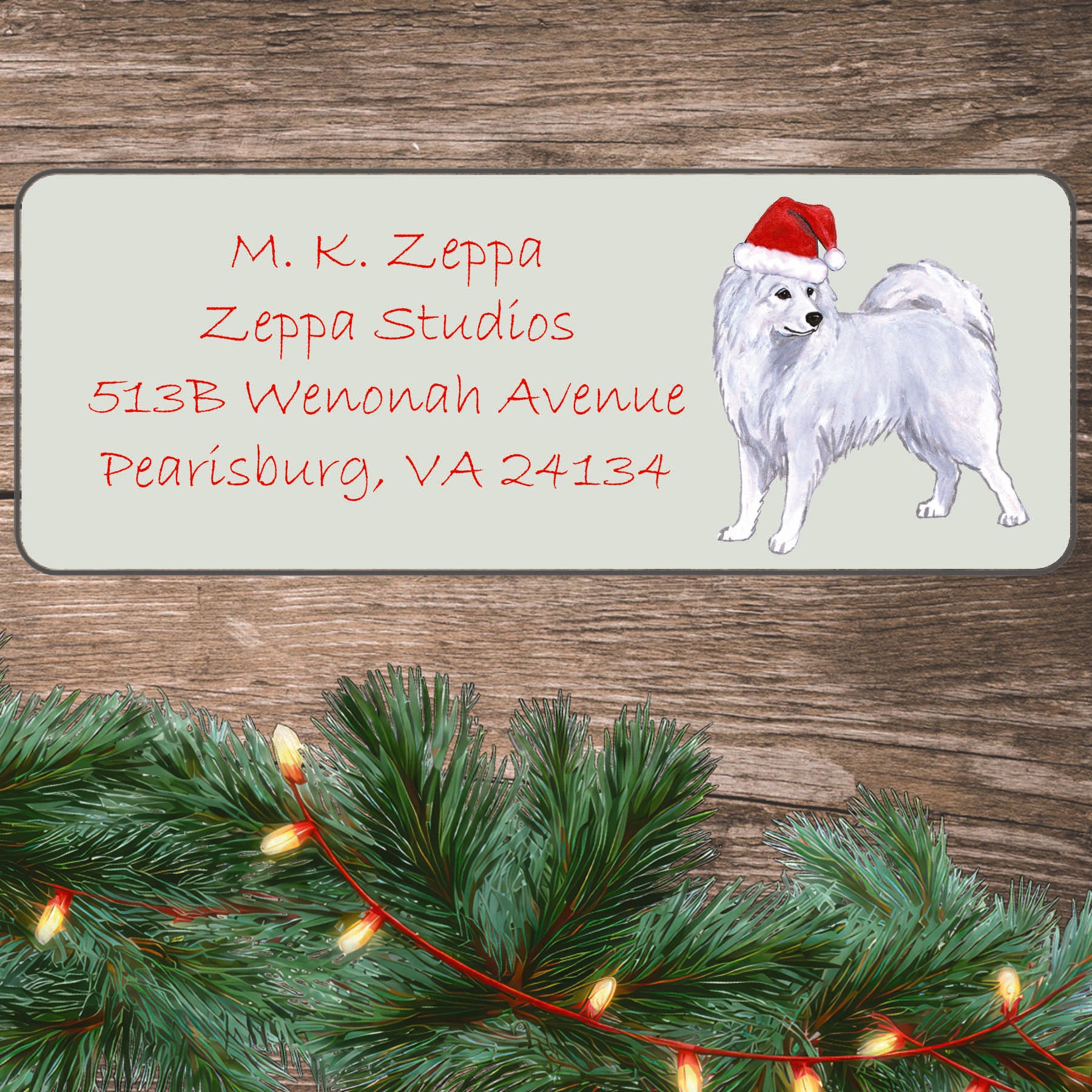 An illustration of a Samoyed dog  wearing a Santa Hat on an ivory return address label set off by a wood surface with holiday greenery background.