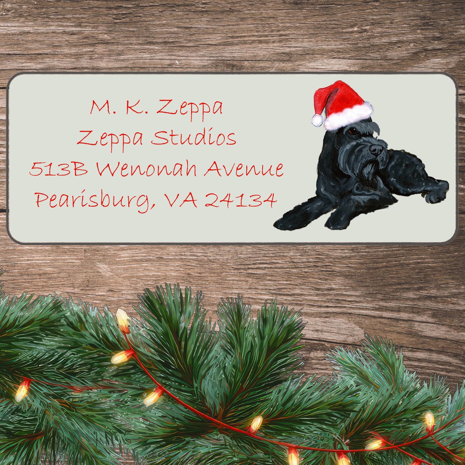 An illustration of a black Schnauzer wearing a Santa Hat on an ivory return address label set off by a wood surface with holiday greenery background.